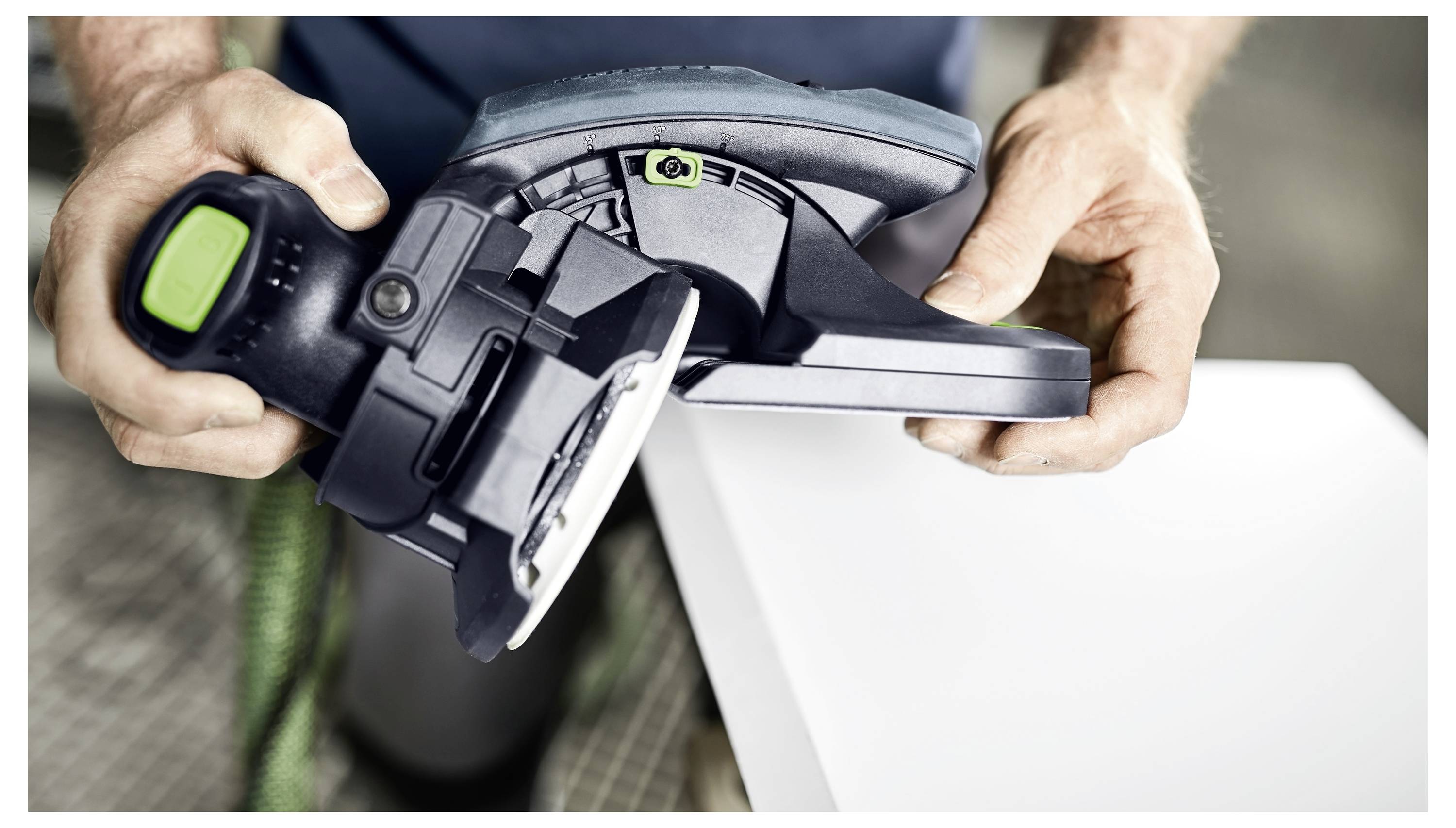 Osoba koja koristi električni alat na bijelog podloge, fokusirajući se na ruke i alat.