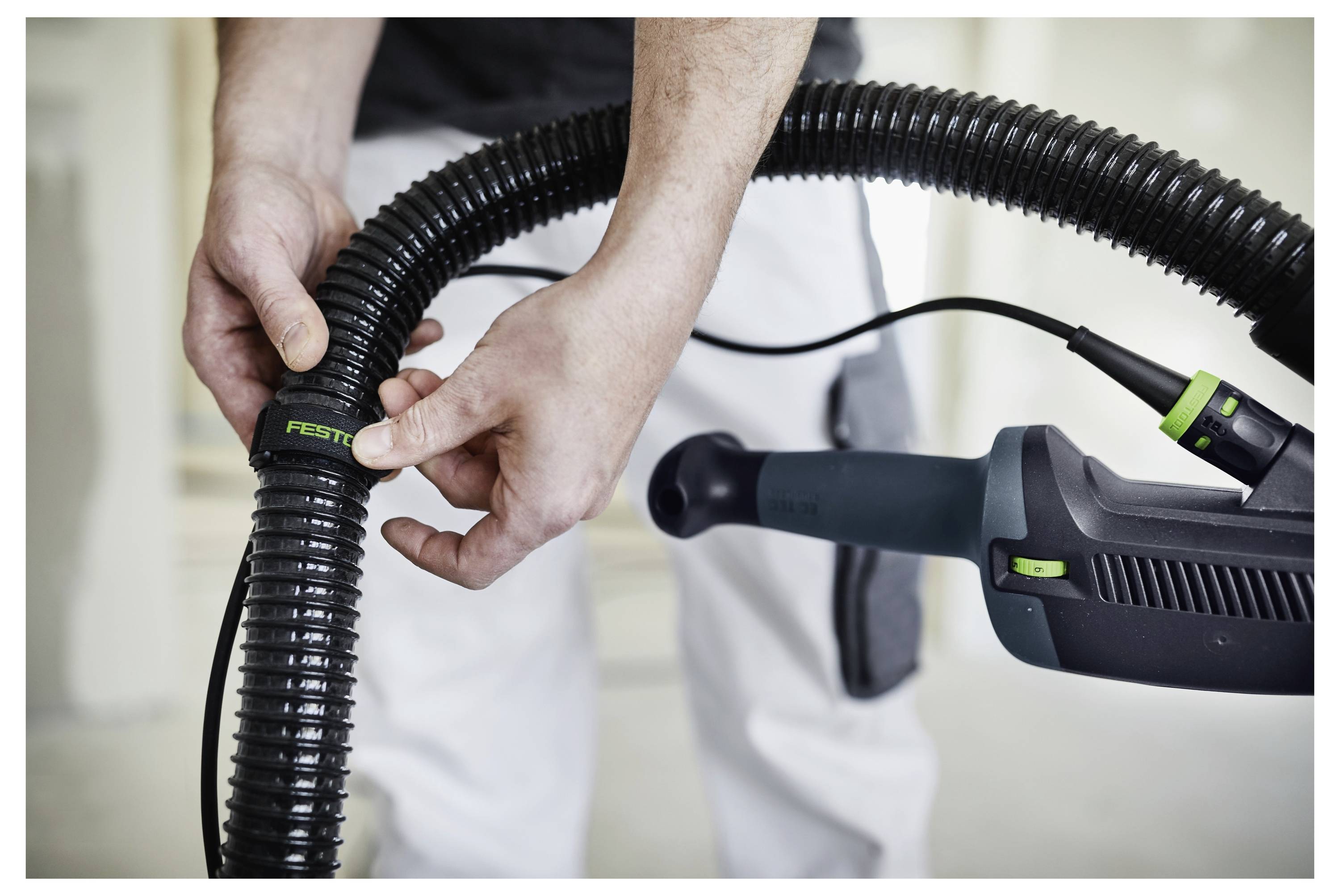 'Osoba priključuje crevo marte Festool na alat, demonstrirajući postavljanje opreme za građevinske ili aktivnosti poboljšanja doma.'