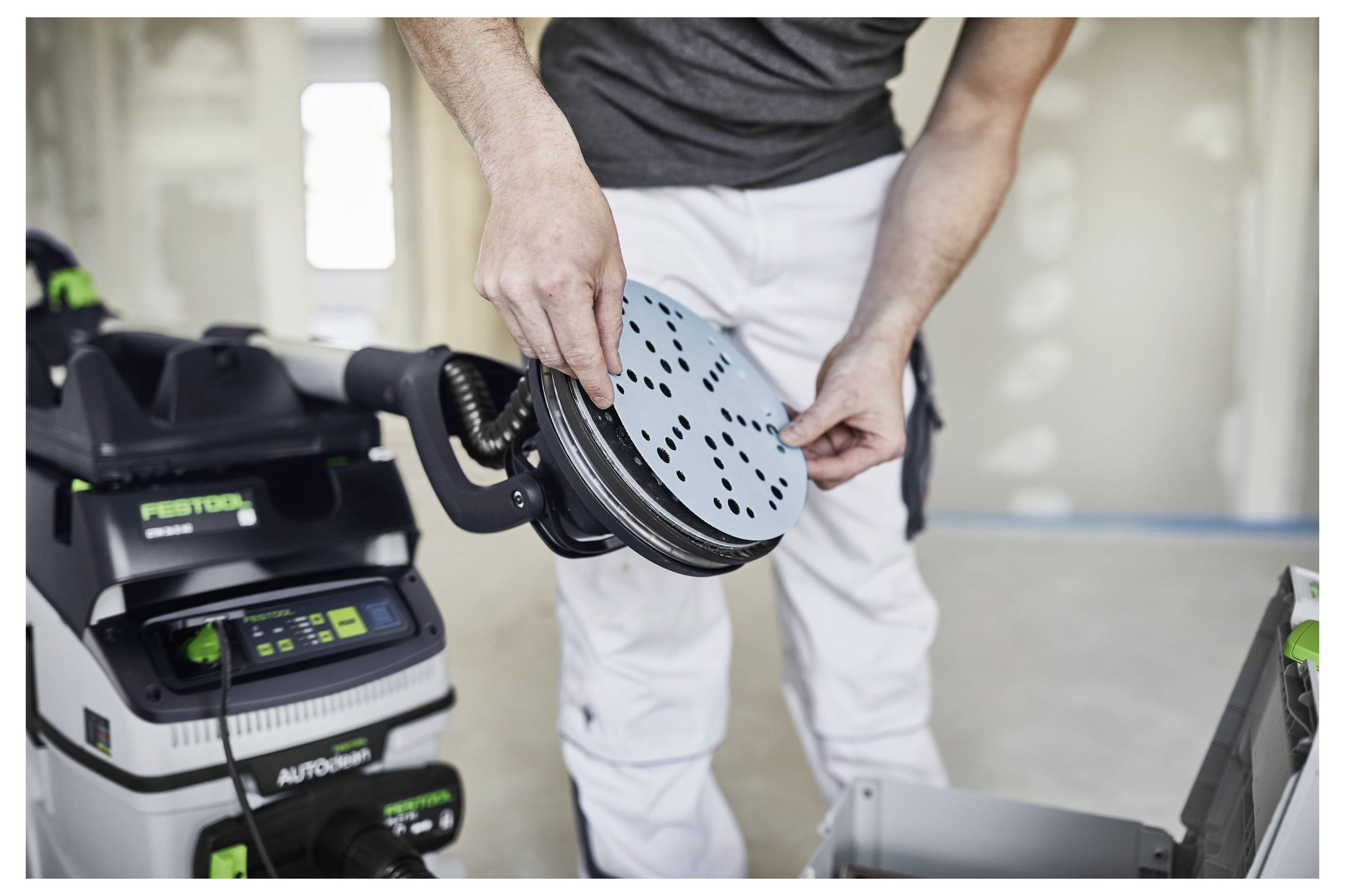 Osoba regulira disk za brušenje na Festool brusilici u okruženju za gradnju ili renovaciju, noseći zaštitnu radnu odjeću.