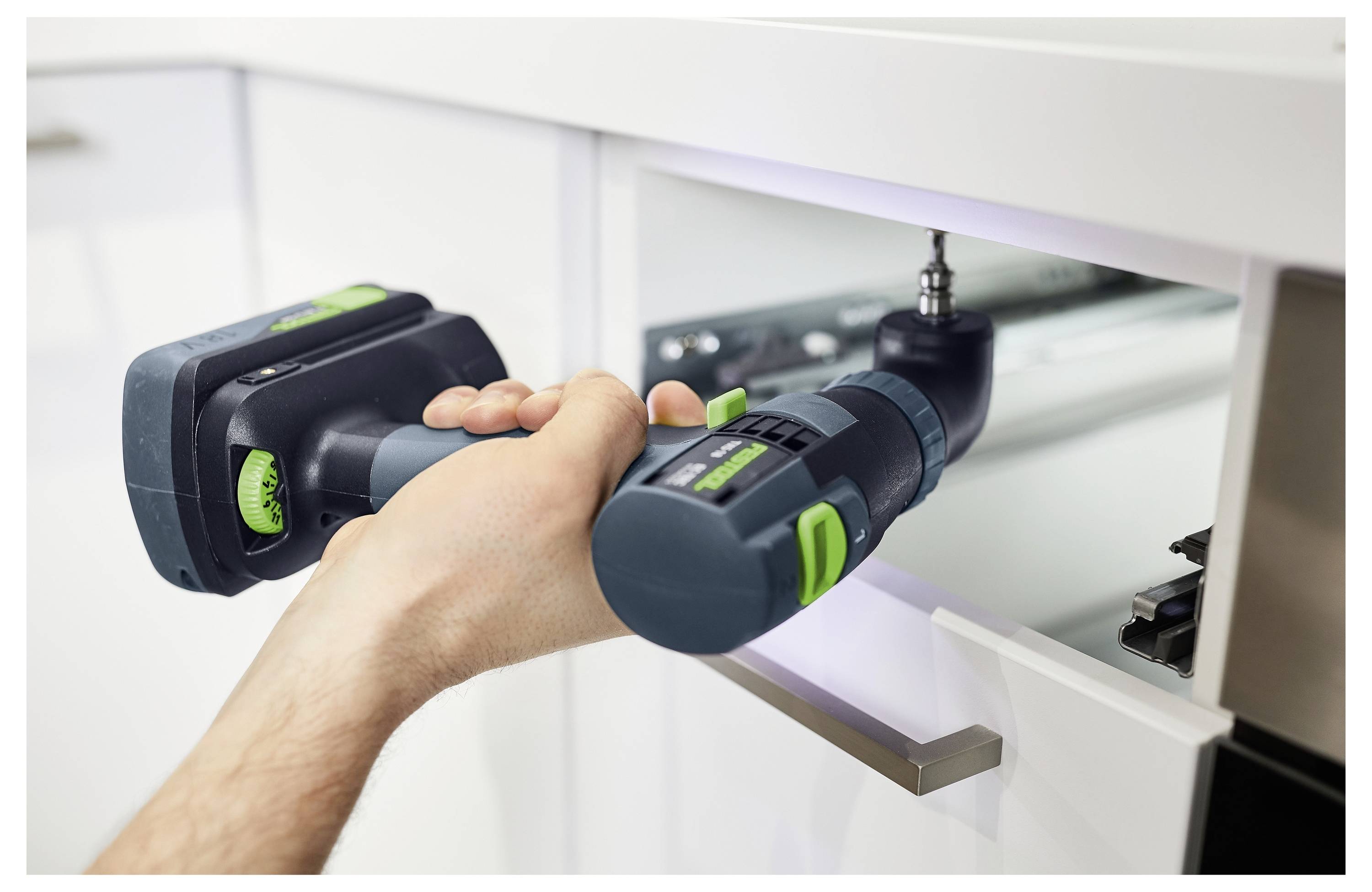 Osoba koristi električnu bušilicu kako bi ugradila vijak u fioku kuhinjskog ormarića, što pokazuje DIY zadatak za poboljšanje doma.