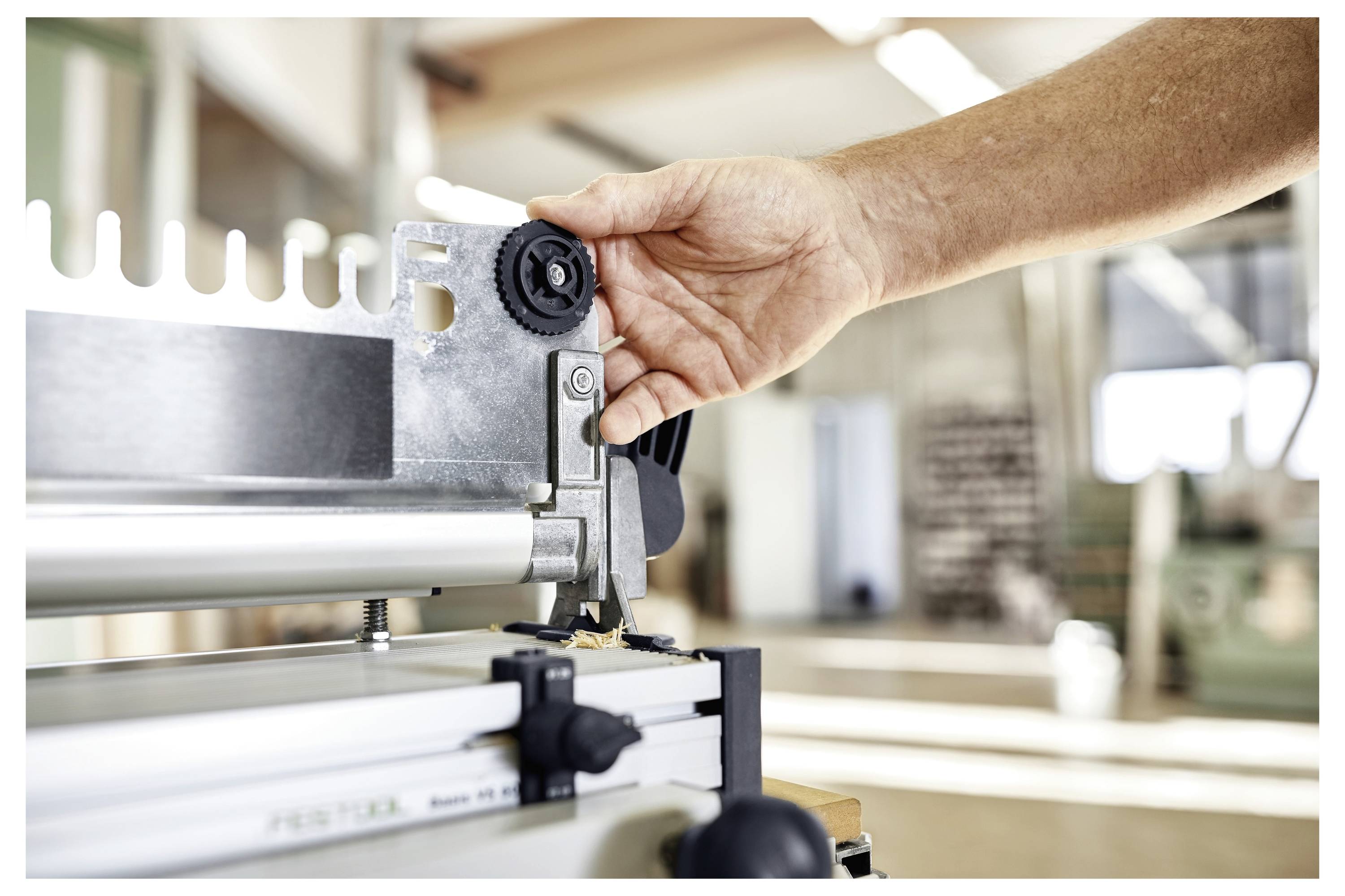 Osoba prilagođava stolarski alat u radionici, fokusirajući se na precizno postavljanje oštrice s rukom na regulacijskoj ručici.