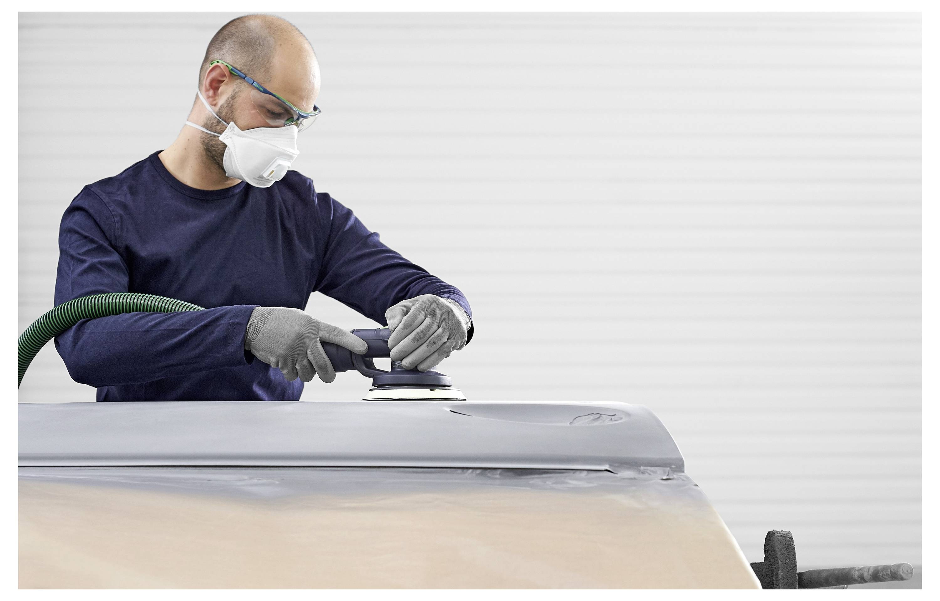 Osoba koja nosi zaštitne naočale i masku brusi veliku, ravnu površinu električnom brusilom, fokusirajući se na preciznost i glatkoću.