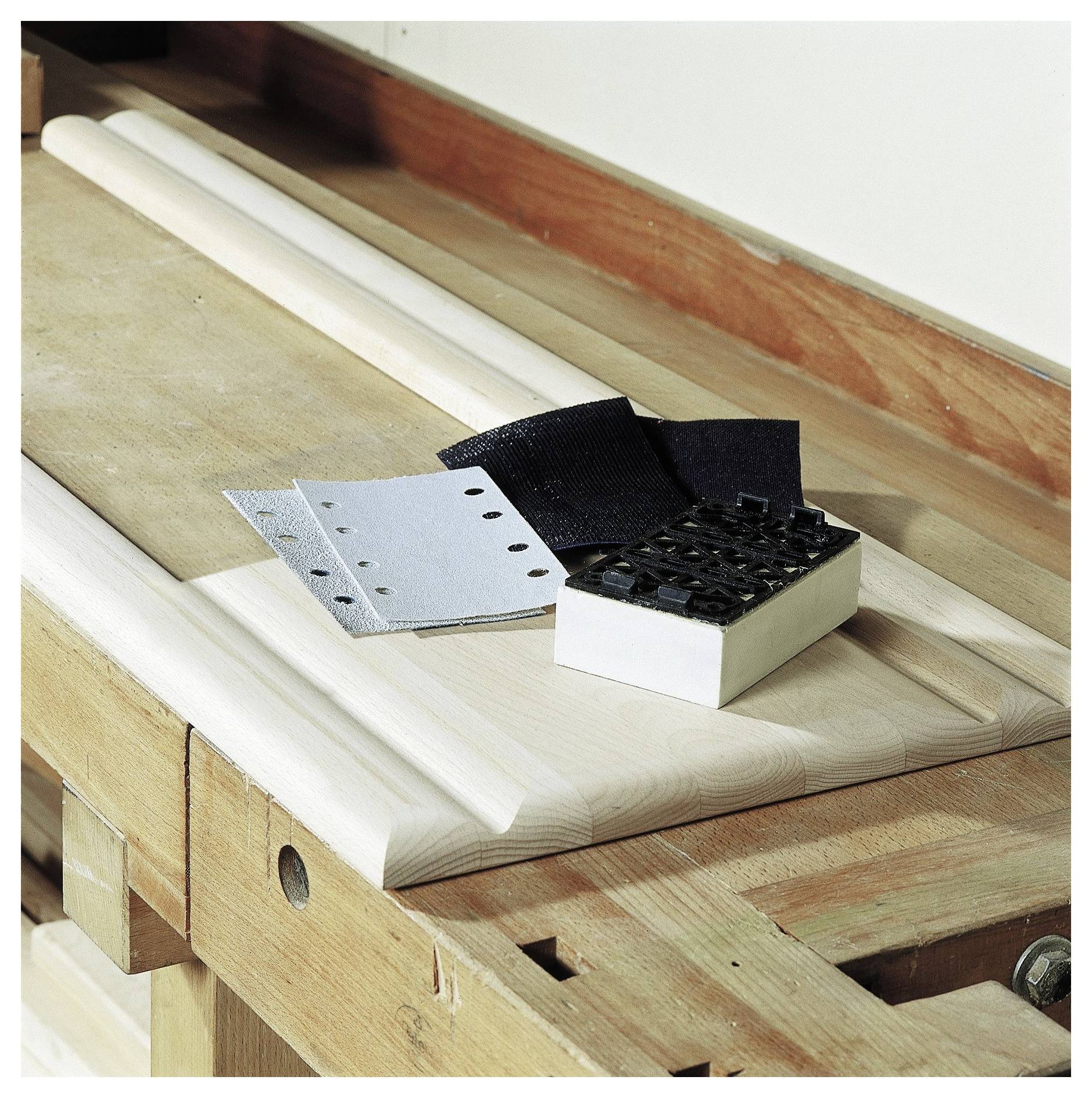 'Alati i materijali za tesarstvo na radnoj klupi, uključujući brusni papir, brusni blok i drvene lajsne, spremni za izradu.'