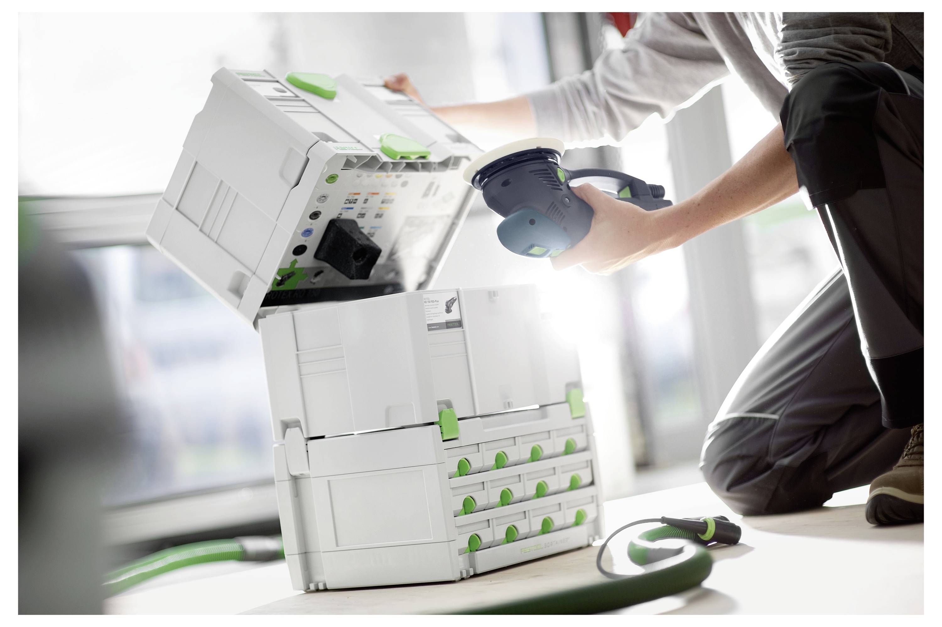 Osoba koja koristi alat sa sustavom modularnog skladištenja u bijeloj i zelenoj boji u blizini, naglašavajući organizaciju i učinkovitost u radnoj radionici.