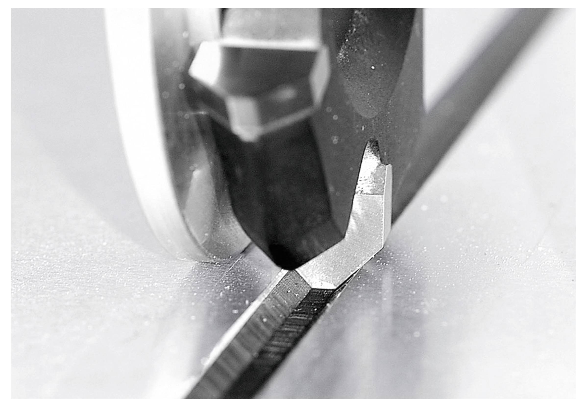 Blizak pogled na oštar nož koji pravi precizan rez duž ruba metalne površine, ističući preciznost rezanja u strojevima.