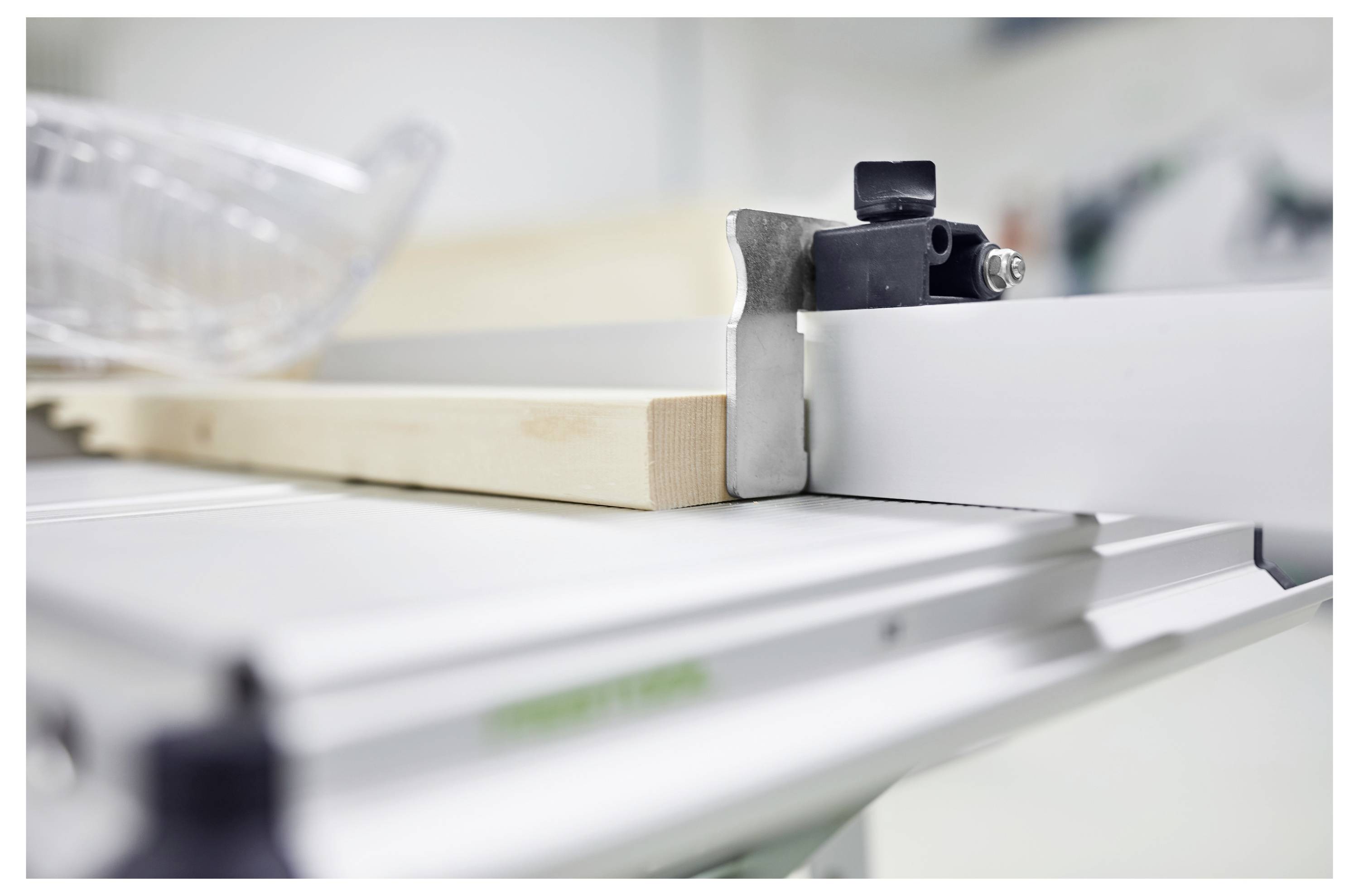 Snimak iz blizine tračne pile koja reže komad drva, s djelomično vidljivim noži i zaštitnom opremom u blizini. Okruženje je radionica.