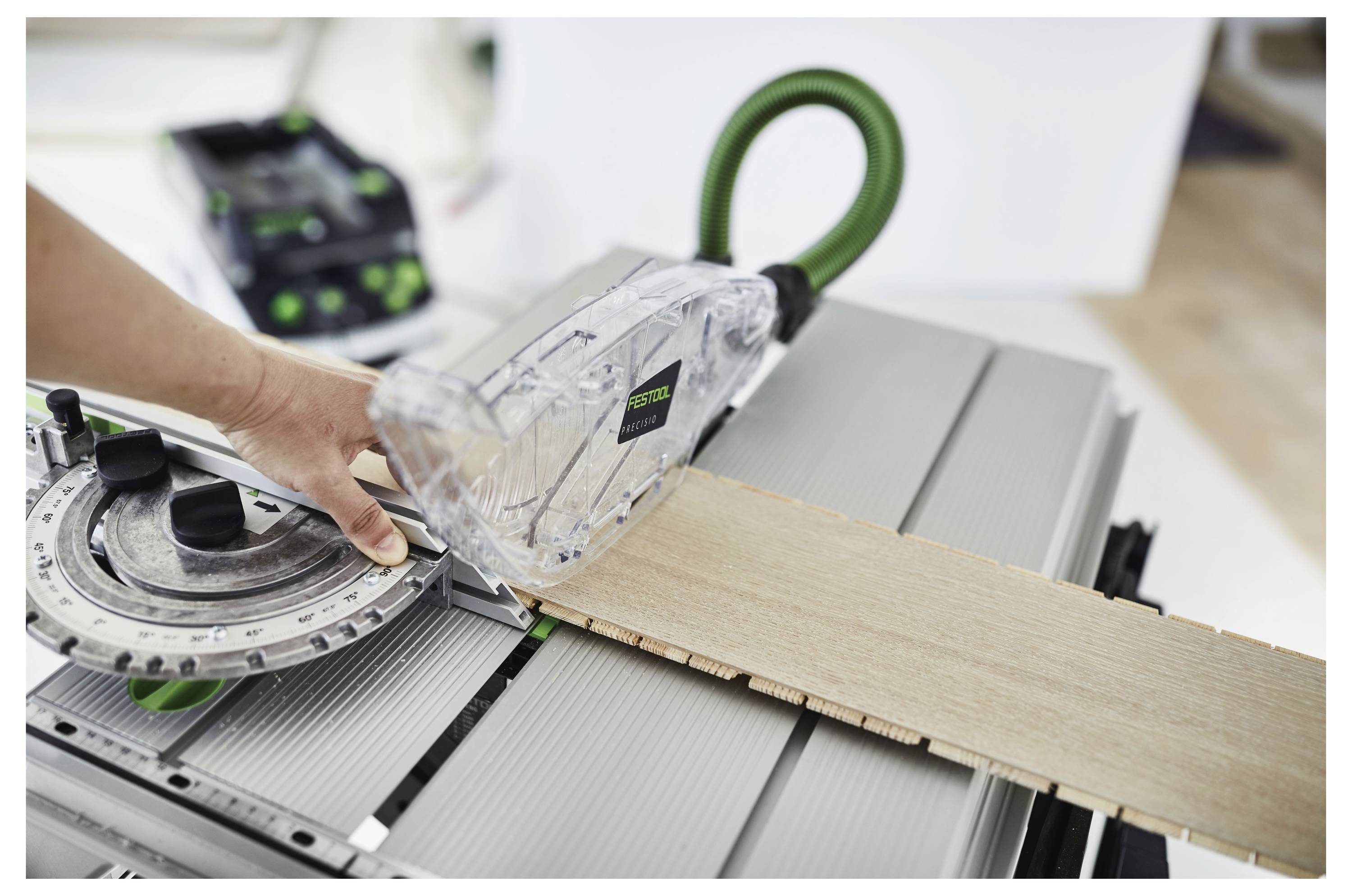 Osoba koristi kružnu pilu s vodilnom tračnicom za rezanje drvene daske. Pila je opremljena sustavom za usisavanje prašine.