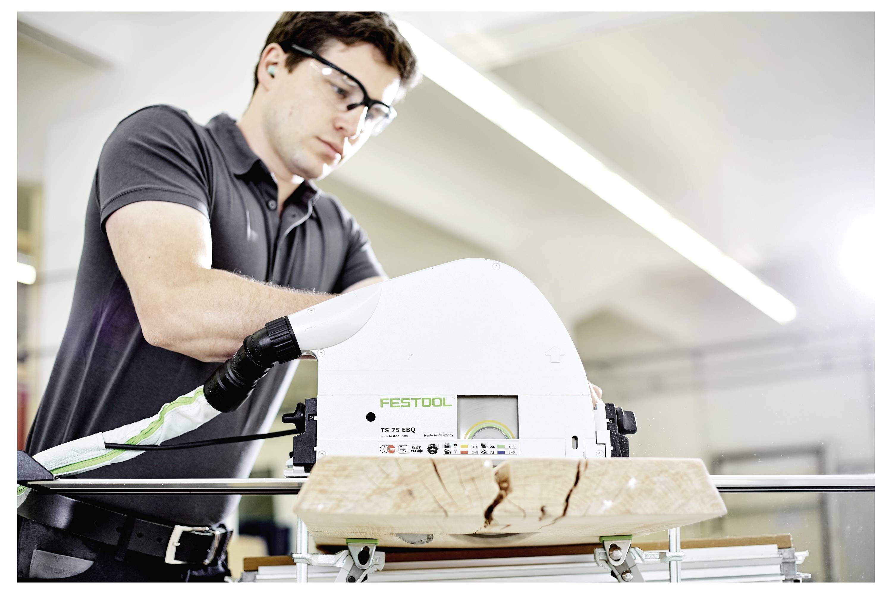 Osoba koja nosi zaštitne naočale upravlja kružnom pilom Festool TS 55 RQ, rezanjem komada drva na radnom stolu u radionici.