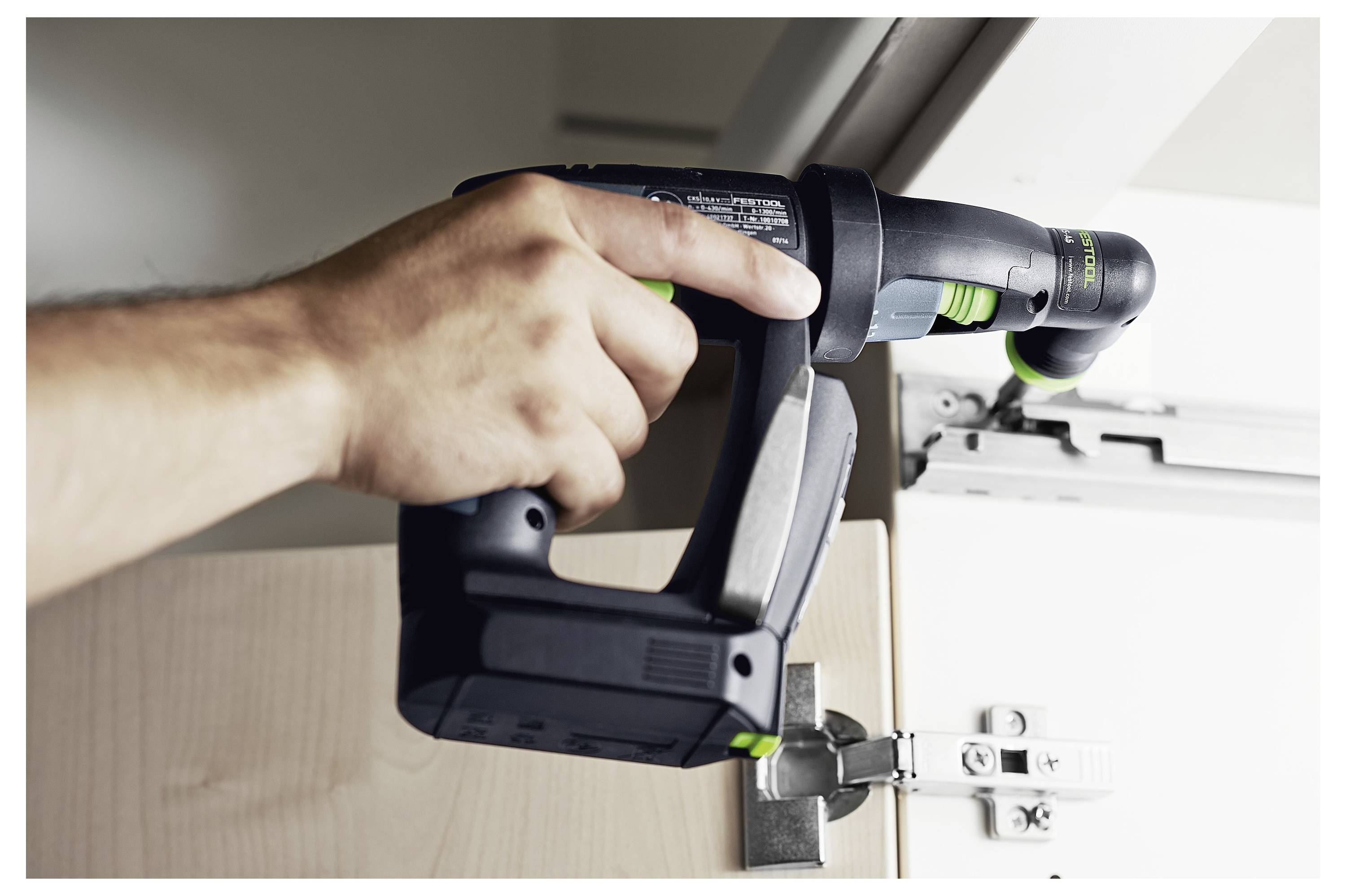 Osoba koristi bušilicu za podešavanje pant za vrata ormarića, što ističe zadatak unaprijeđenja doma.