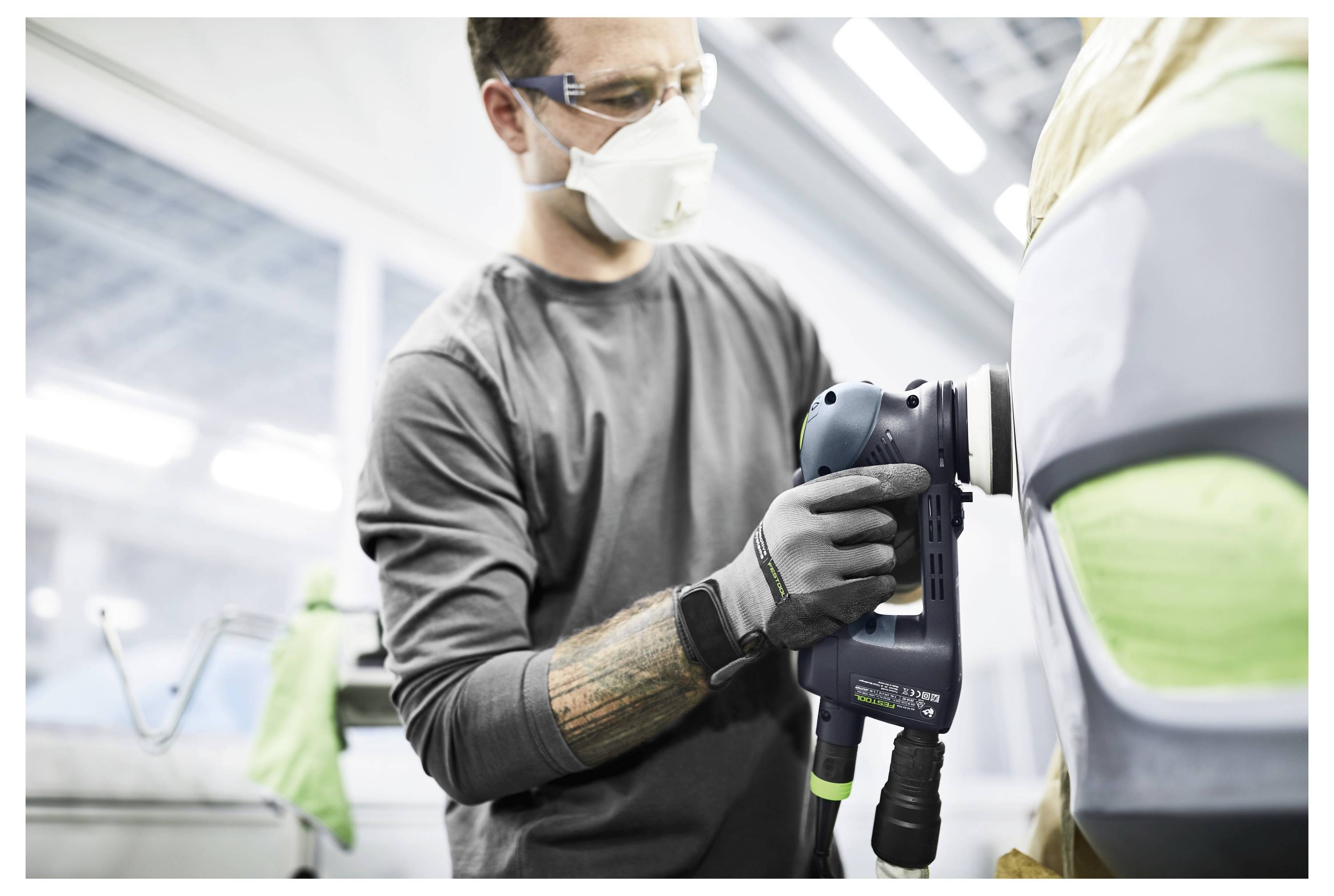 Osoba koja nosi masku i rukavice koristi električni alat za brušenje vozila u radionici, naglašavajući sigurnost i preciznost u automehaničarskim radovima.