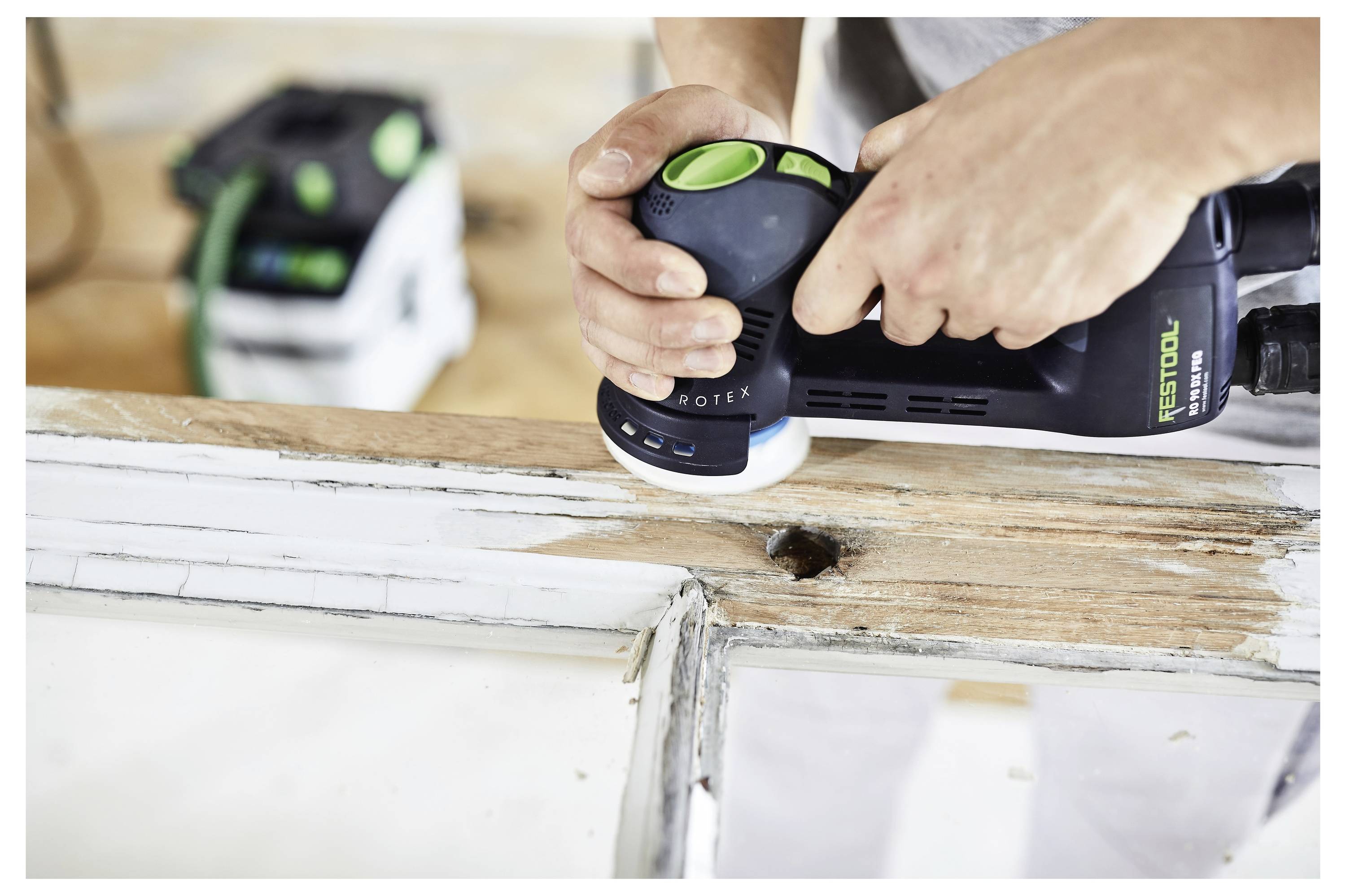 Osoba koristi električnu brusilicu za izglađivanje drvenog okvira prozora, fokusirajući se na uklanjanje stare boje i izglađivanje površine.