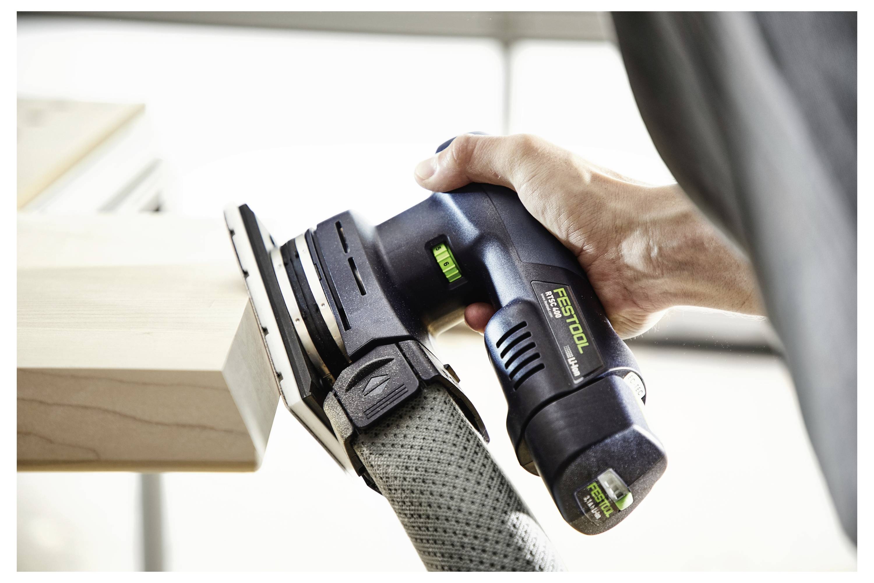 Osoba koristi ručnu električnu brusilicu da ugladi rub drvene ploče, što ukazuje na projekt stolarstva ili popravku "uradi sam".