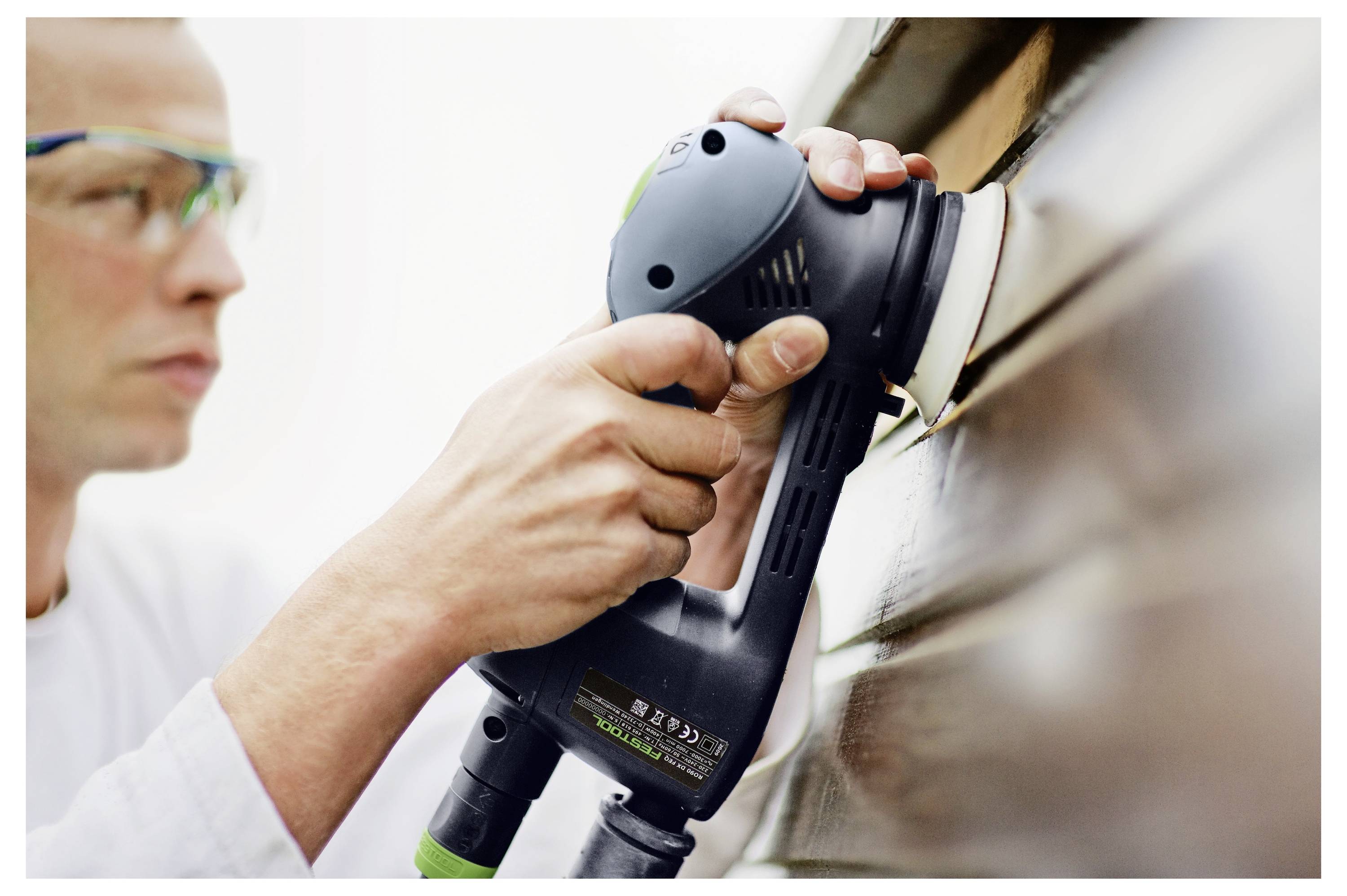 Osoba koristi elektricni brusilica da ugladi drv enu povr inu, nosec i zatitne naocale za zastitu.