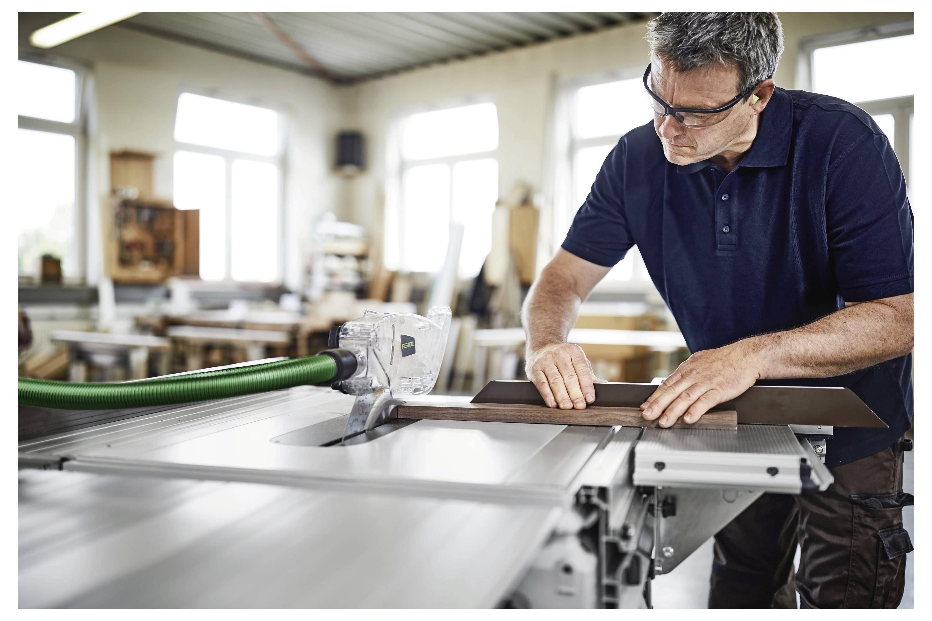 Čovjek koji nosi zaštitne naočale i rukavice koristi električnu bušilicu na betonskom zidu, ističući sigurne gradilišne prakse.