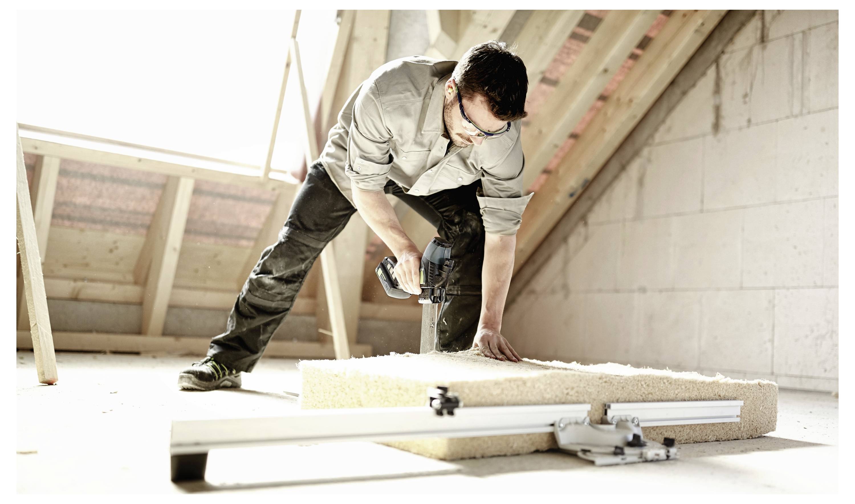 Osoba koristi električni bušač na komadu izolacije na potkrovlju, pokazujući nedovršene radove na obnovi kuće.