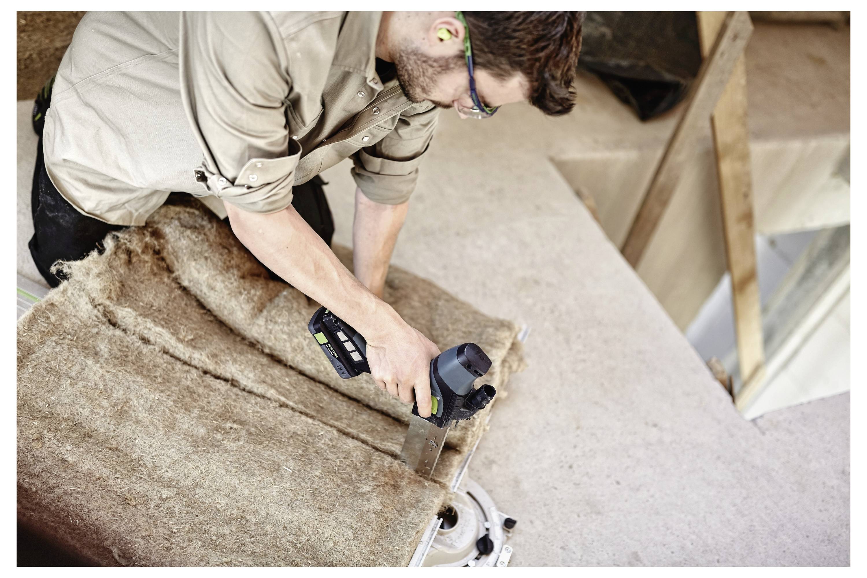 Osoba koja koristi alat za rezanje izolacijskog materijala na mjestu gradnje. Nosi naočale i zaštitu za uši radi sigurnosti.