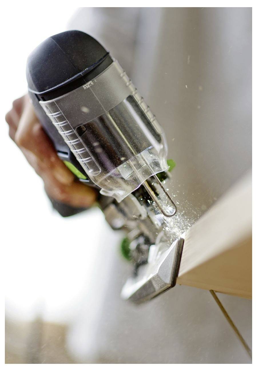 Osoba upravlja tračnom pilom, rezanjem kroz drvenu dasku, stvarajući piljevinu. Alat je nagnut, pokazujući aktivnost u obradi drva.