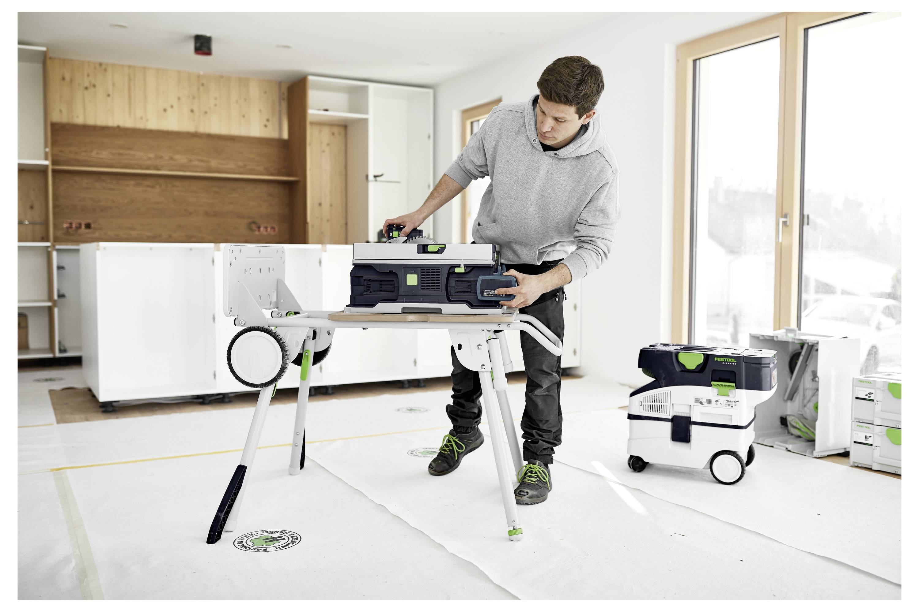 Osoba koja regulira postavke na bežičnoj bušilici, stojeći pored drvene ljestve u dobro osvijetljenoj sobi.