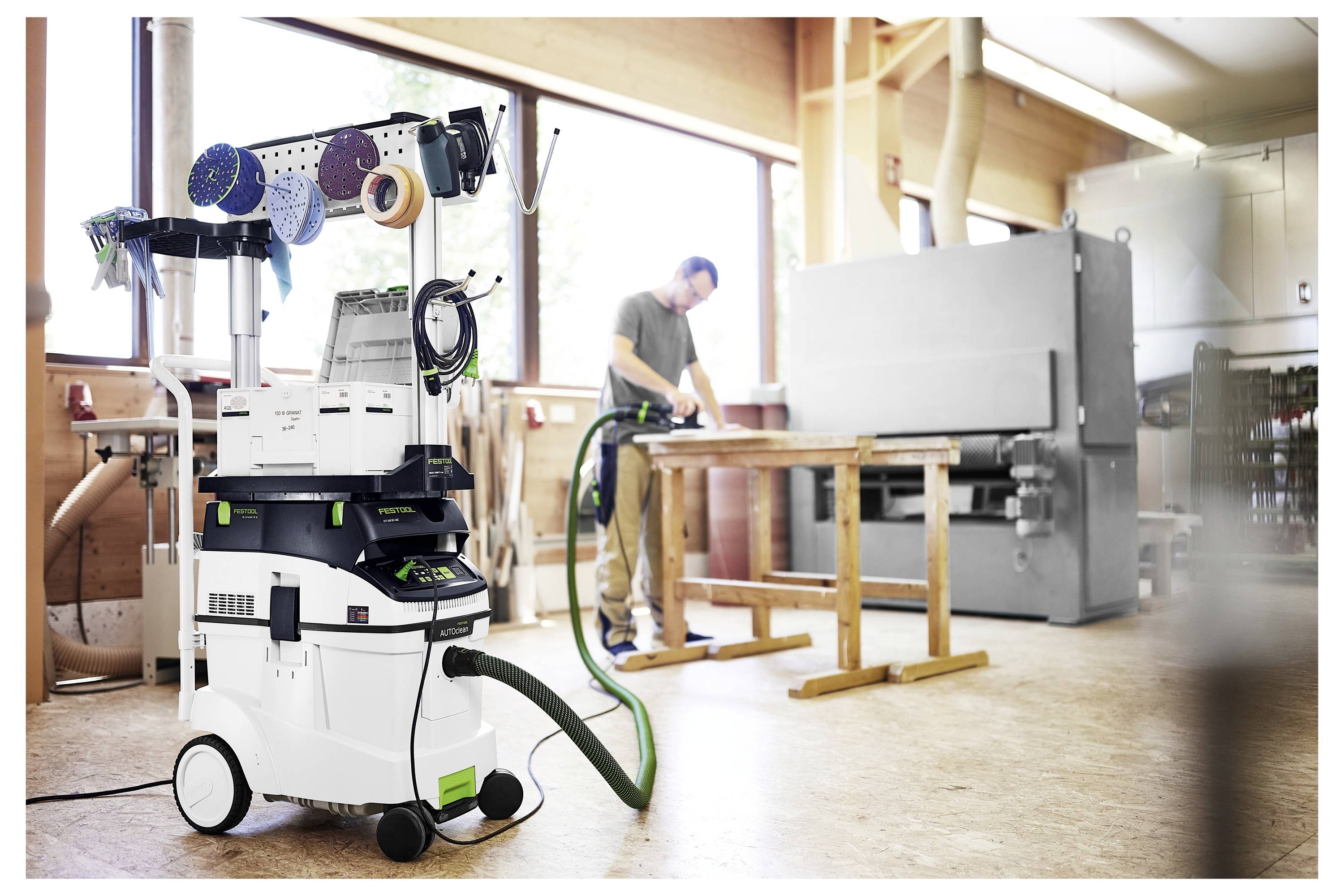 'Radionica sa osobom koja koristi obradu drveta, ekstraktor prašine sa alatima je u prednjem planu, i prozor s prirodnom svjetlošću.'