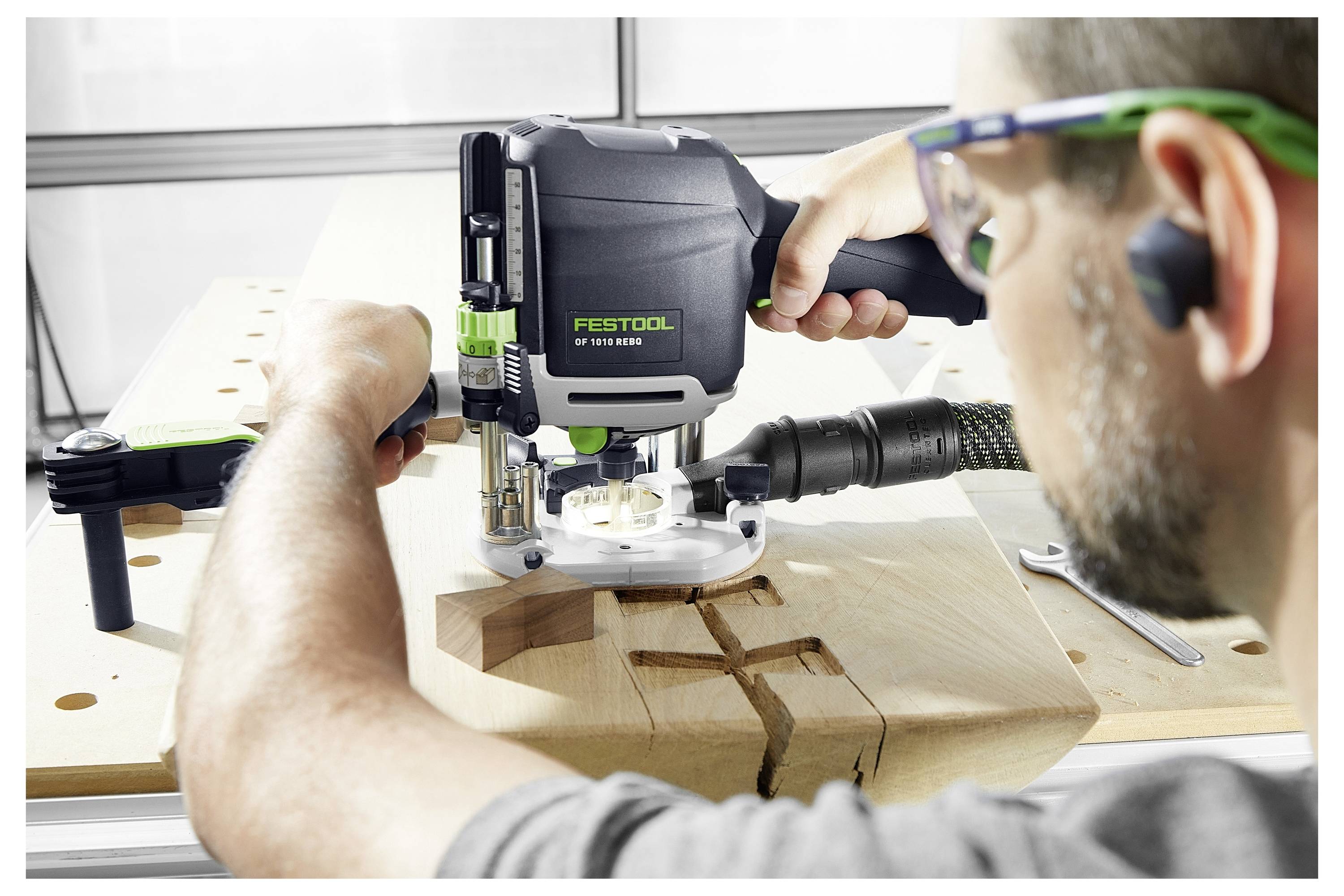 Osoba koristi Festool usmjerivač za rezbarenje preciznog uzorka u drvenu dasku, fokusirajući se na složeno stolarstvo sa zaštitnom opremom.