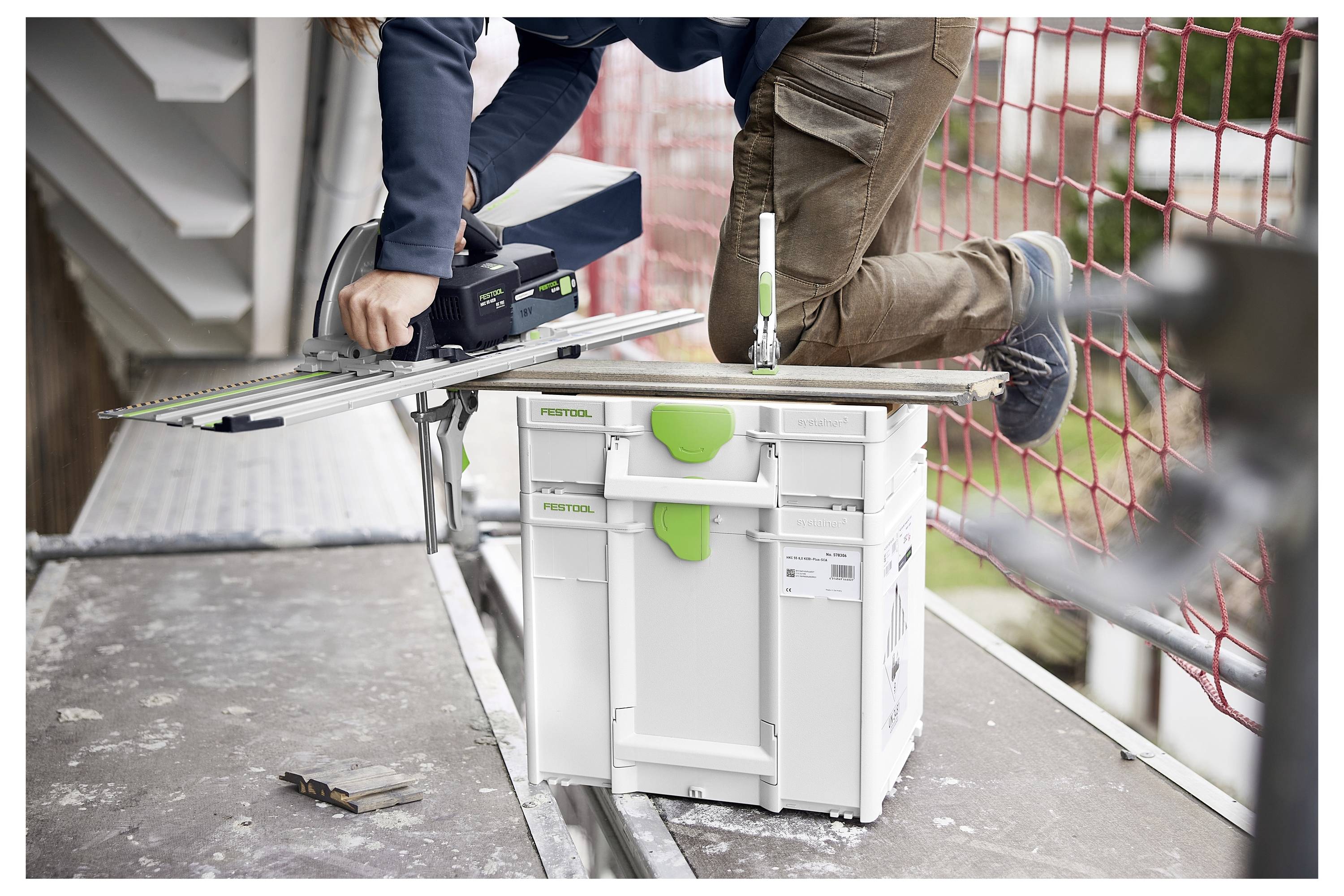 Čovjek u zaštitnim naočalama koristi kružnu pilu za rezanje drvenih dasaka na podu. Vakuum-sličan stroj je prikačen, skupljajući prašinu.