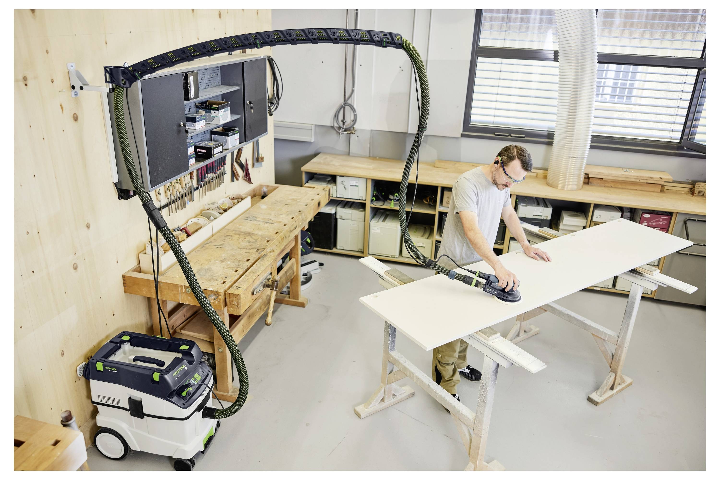 Muškarac u kapi i dugim rukavima stoji u tečaju za obradu drva, okrenut prema policama punim naslaganih drvenih ploča.