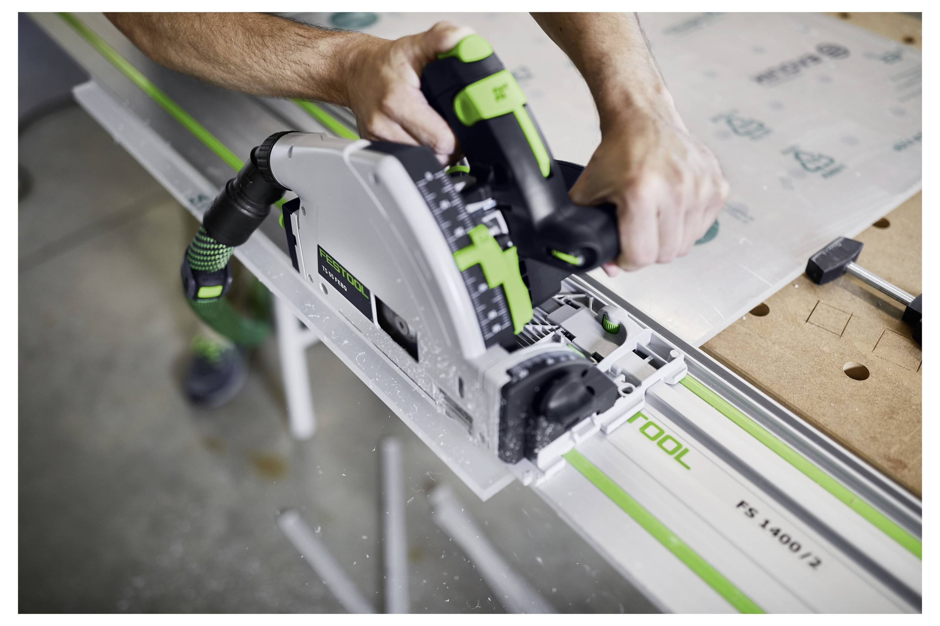 Osoba koristi kružnu pilu za rezanje duž vodiče na radnom stolu. Pila je obojena u zelenu i bijelu boju.