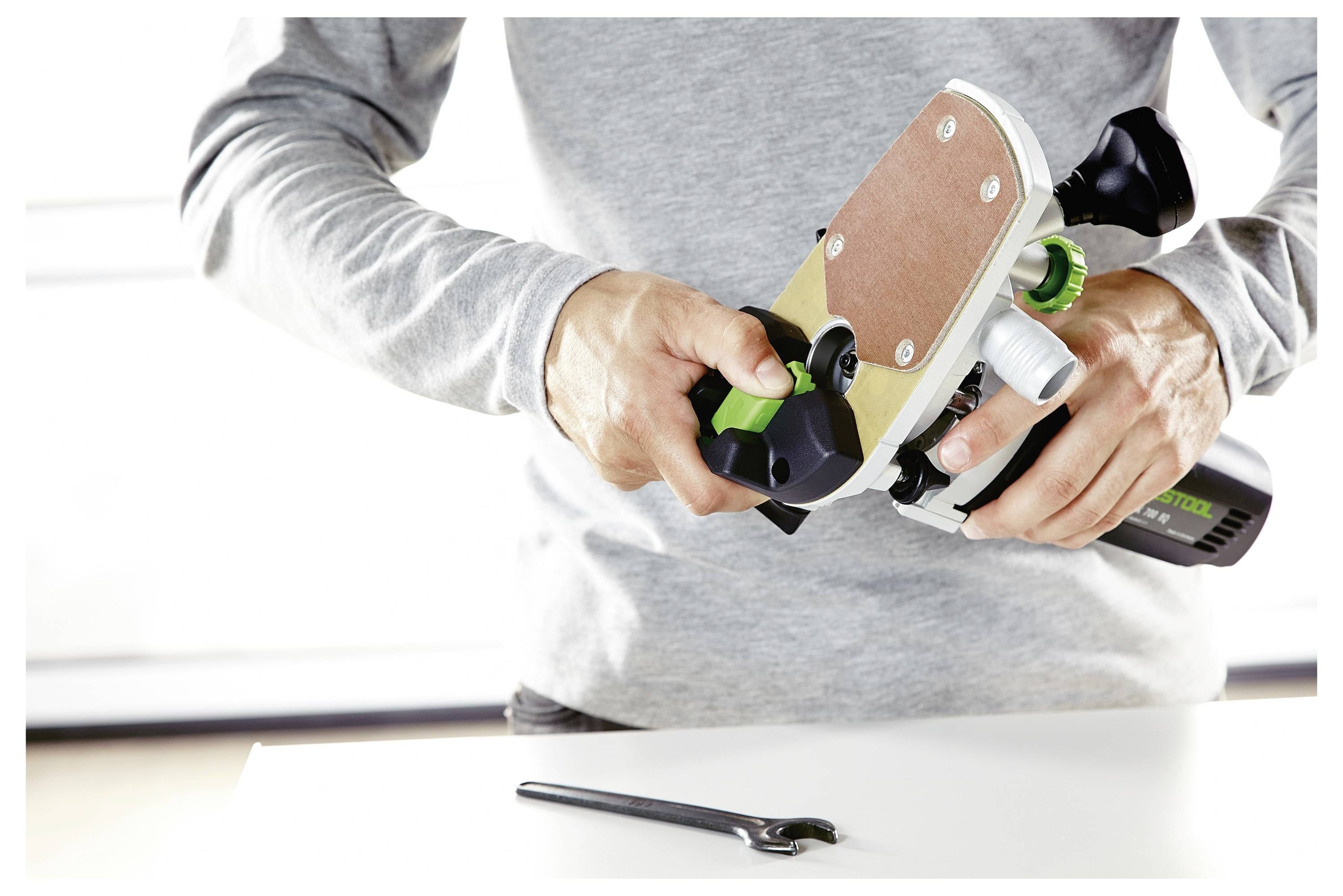 Osoba podešava stolarsku alatku na stolu, s ključem u blizini, što sugeriše održavanje ili postavljanje alata.