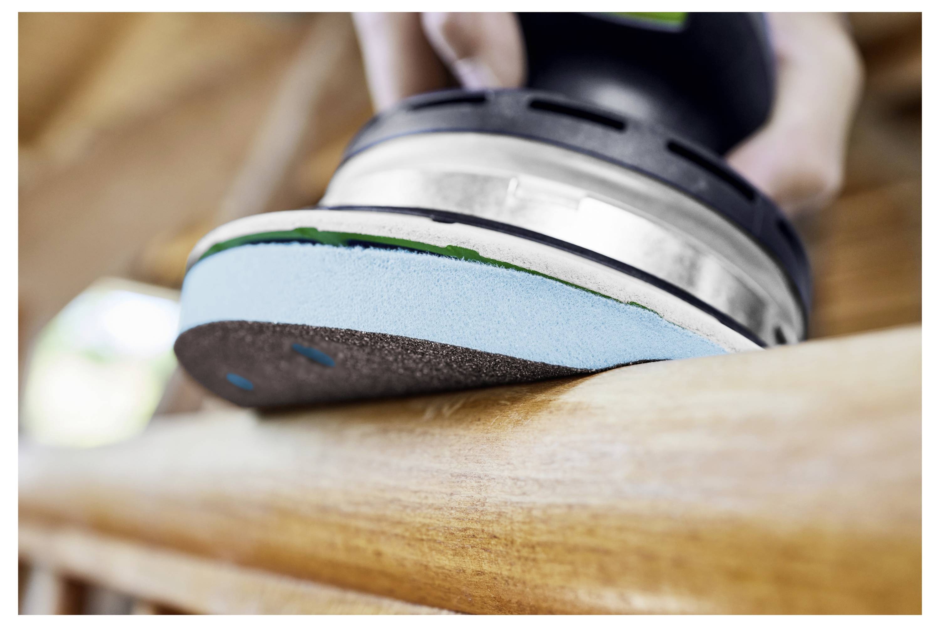 Ručni električni brusilica gladi površinu drva, pokazujući bliski prikaz alata u radu, ističući njegovu granulaciju i dizajn.