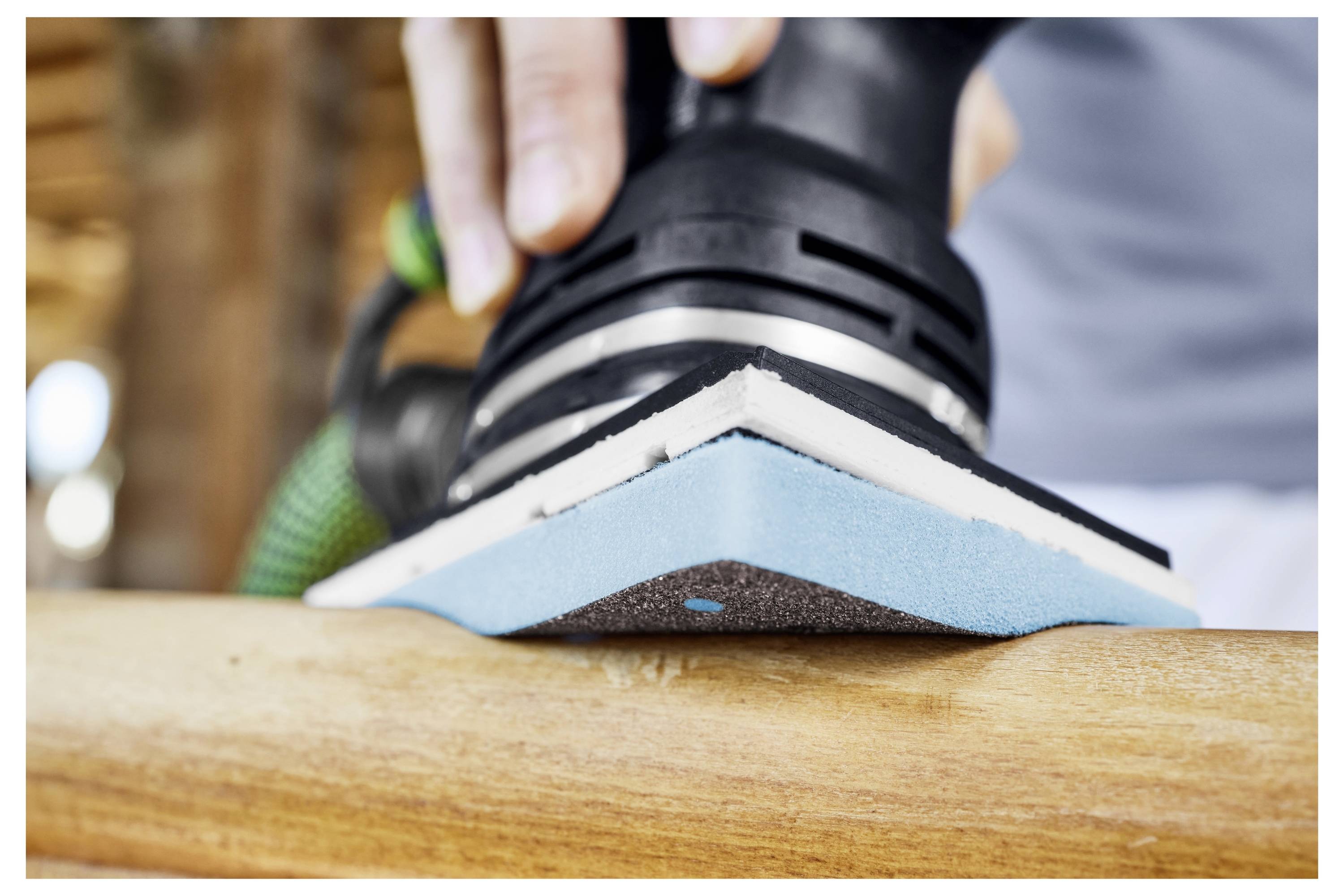 Osoba koristi električni brusilica na drvenu površinu, gladeći je za završnu obradu. Fokus je na brusilici i teksturi drva.