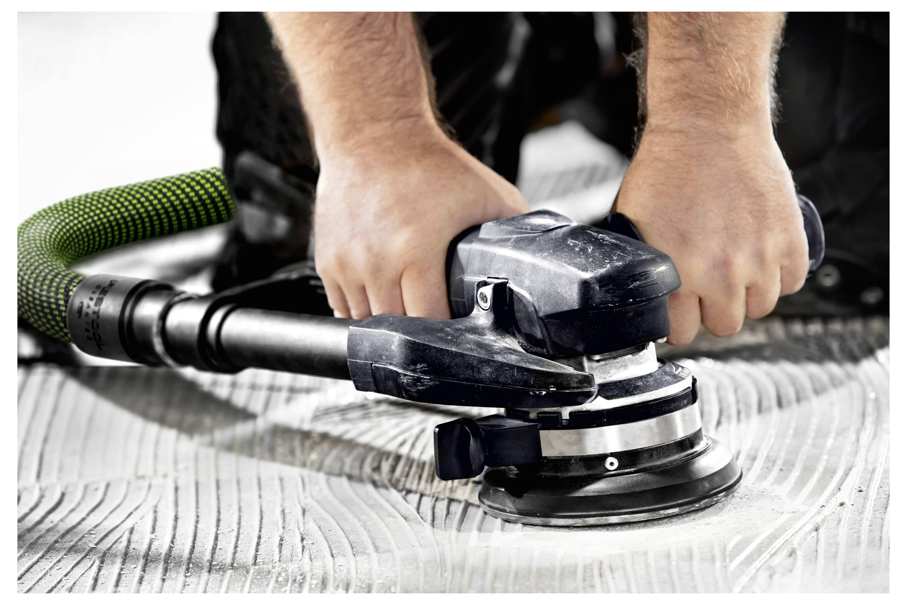 Ruke drže brusilicu snage koja gladi drvenu površinu. Vakuumska prihvatnica prikuplja prašinu, prikazujući stolarstvo u tijeku.