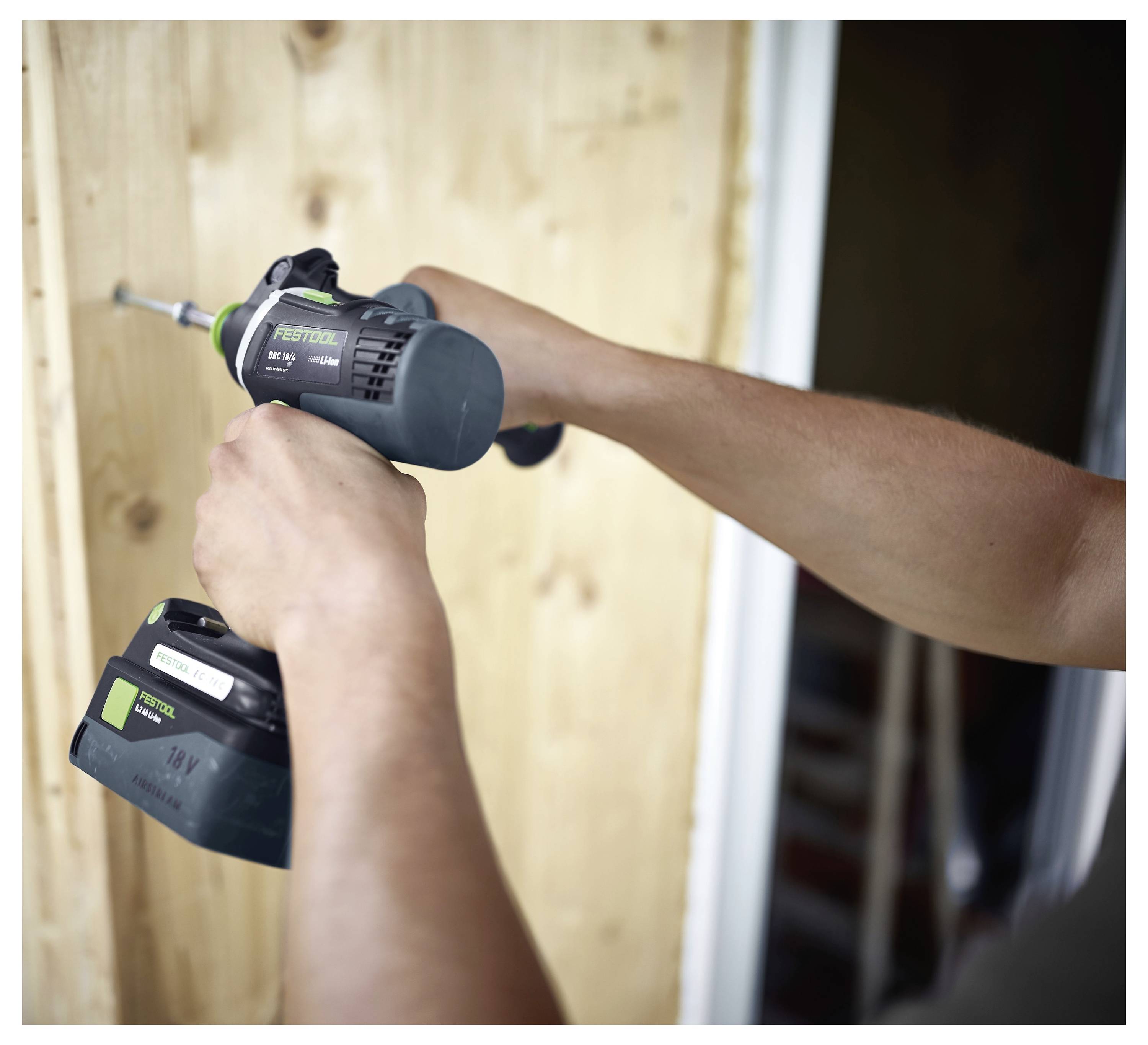 Osoba koristi bežičnu bušilicu za vijčanje u drvenu dasku blizu vrata, demonstrirajući DIY gradnju ili popravni radovi.
