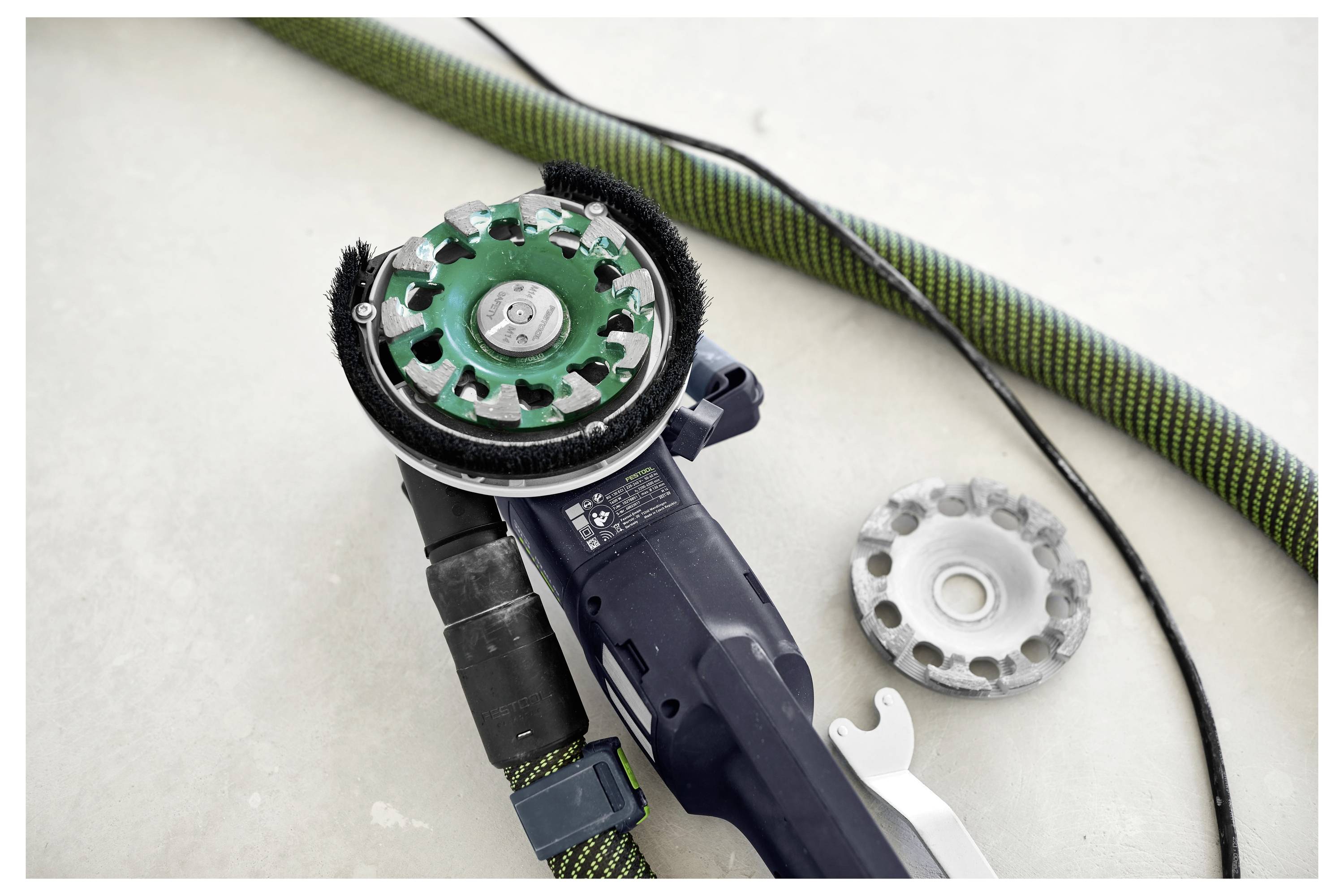 Radnik na gradilištu u zaštitnoj opremi koristi bušilicu na drvenom okviru na mjestu gradnje, s gradilišnim skhelama u pozadini.