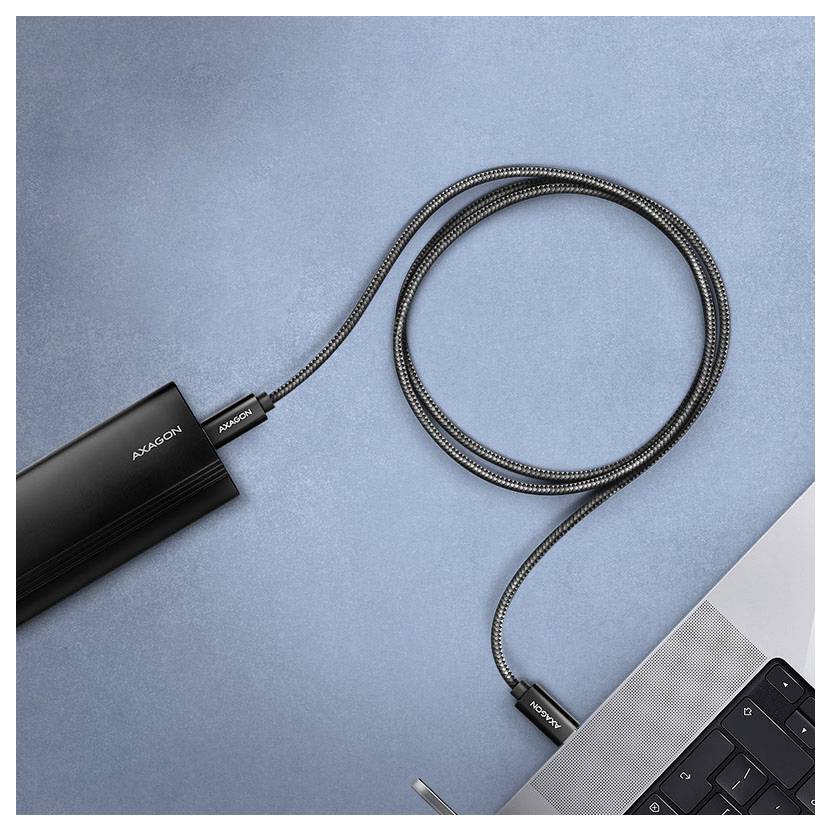 Crni kabel za punjenje marke 'ALXICOON' od prijenosne baterije do prijenosnog računala, na plavoj teksturiranoj površini.