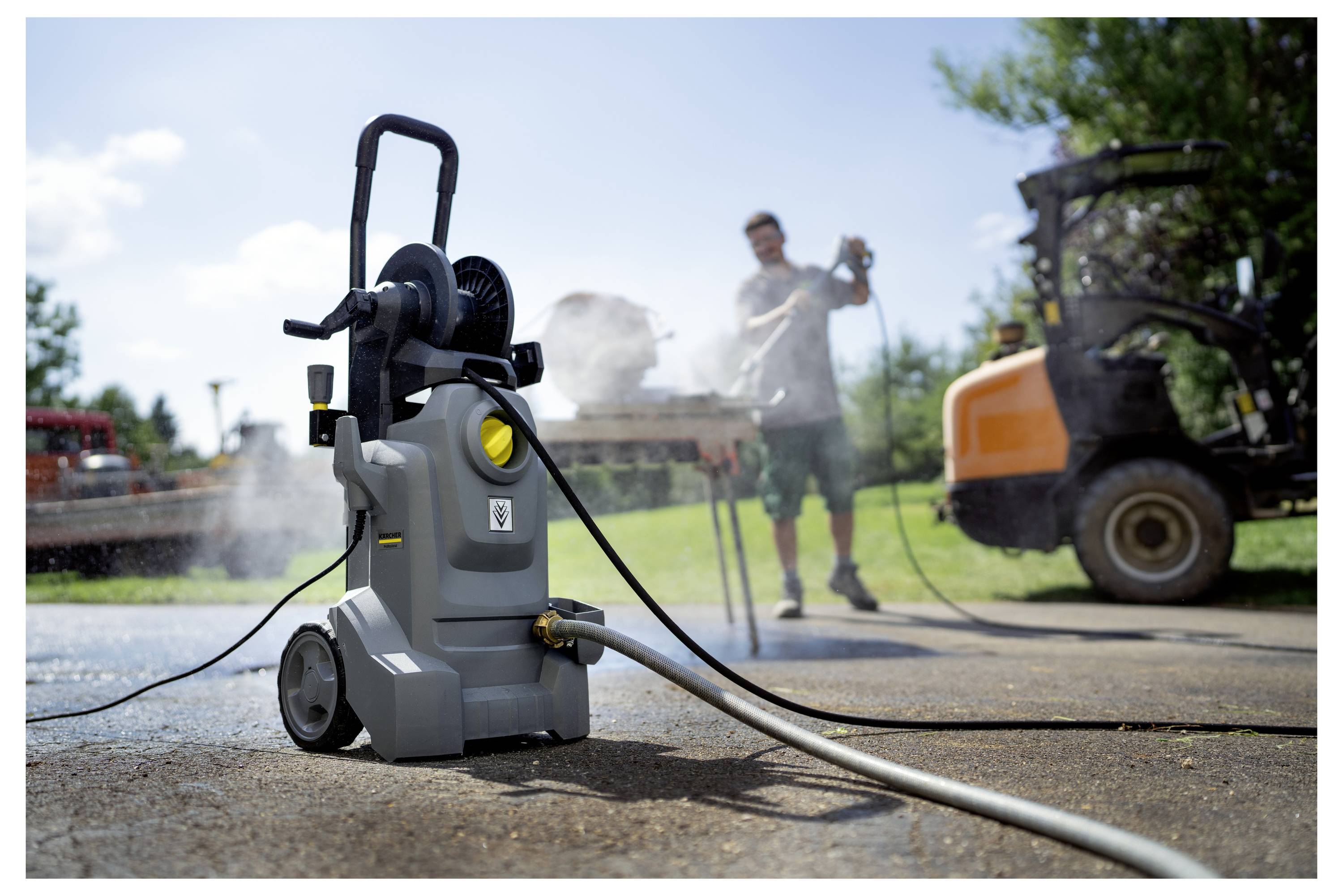 Osoba koristi visokovrski čistač na prilaznoj stazi, s crijevom pričvršćenim na njega. Vozilo i stabla su vidljivi u pozadini.