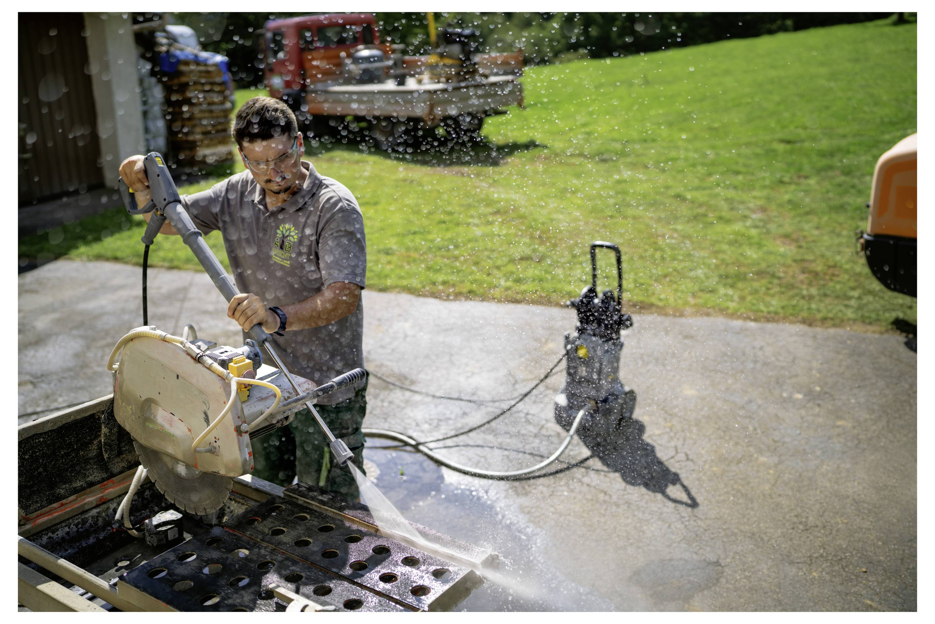 Osoba koristi motoriziranu pilu za rezanje materijala na vanjskoj površini; voda iz pile prska, održavajući područje vlažnim.