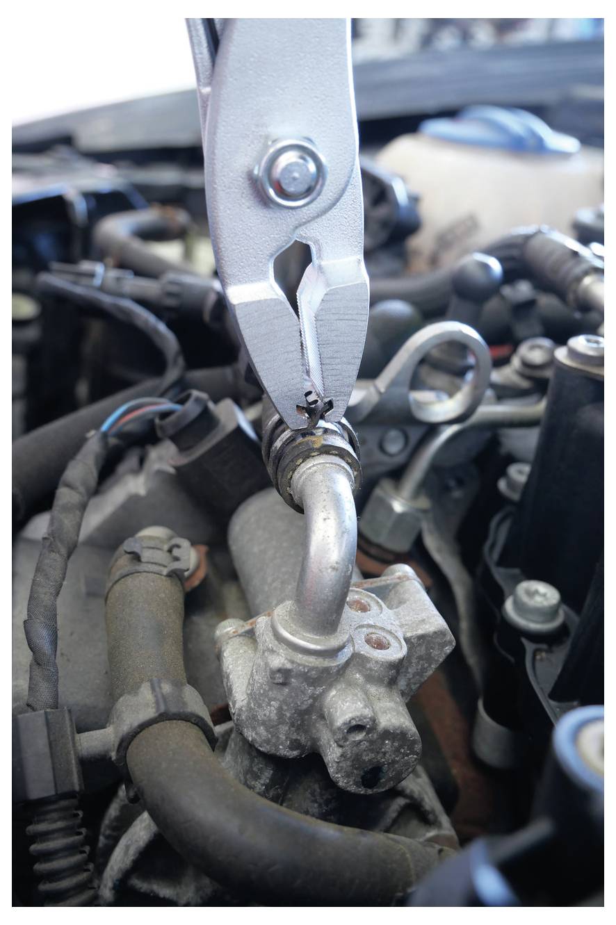 Detaljni prikaz klešta koja stežu metalnu cijev u automobilskom motoru, ističući radove na popravci dijelova vozila.