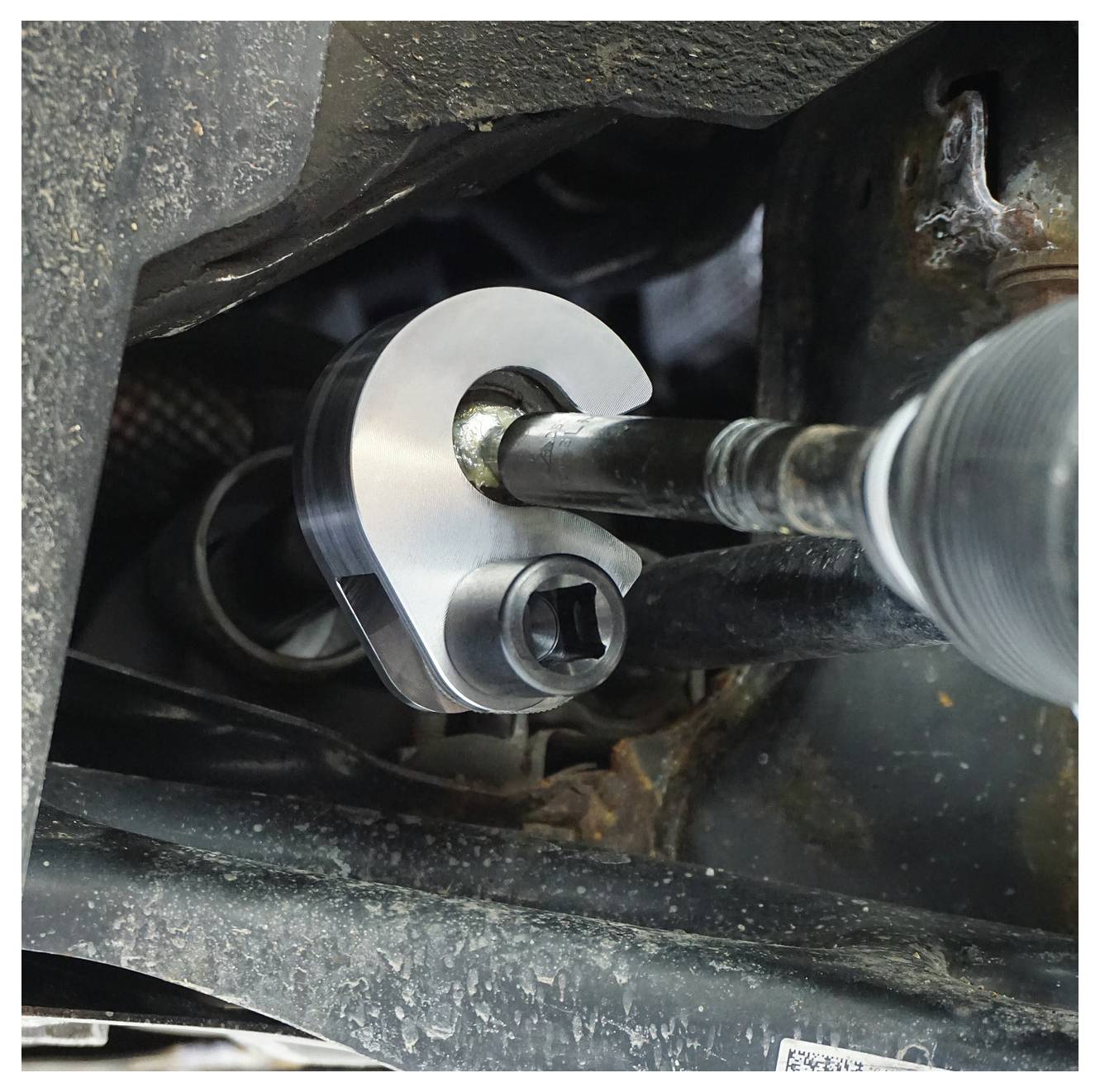 C-oblikovani ključ za moment sile koristi se na vijku kontrolnog kraka vozila, pokazujući uključenost alata za precizno pritezanje.