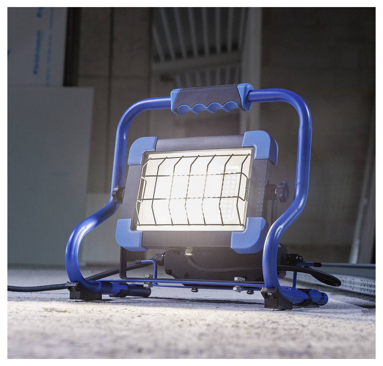 Plava prenosiva reflektorska lampa osvetljava betonski pod u slabo osvetljenom prostoru, ističući njegovu čvrstinu i industrijsku dizajn.