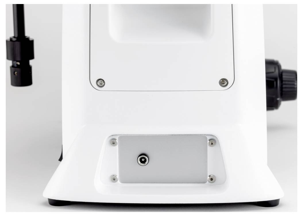 Slika prikazuje stražnju stranu bijele podloge mikroskopa s priključkom za napajanje i vijcima za pričvršćivanje pribora.