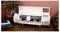 Bijeli elektronski rezač obeležen sa "Siser" stoji na drvenom stolu, okružen knjigama, lončićima sa biljkama i dekorativnim predmetima.