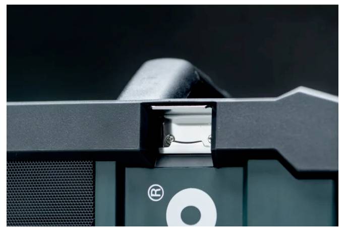 Detaljni snimak uređaja koji pokazuje priključak u sredini, okružen crnom kućištem s djelomično vidljivim simbolom 'R'.