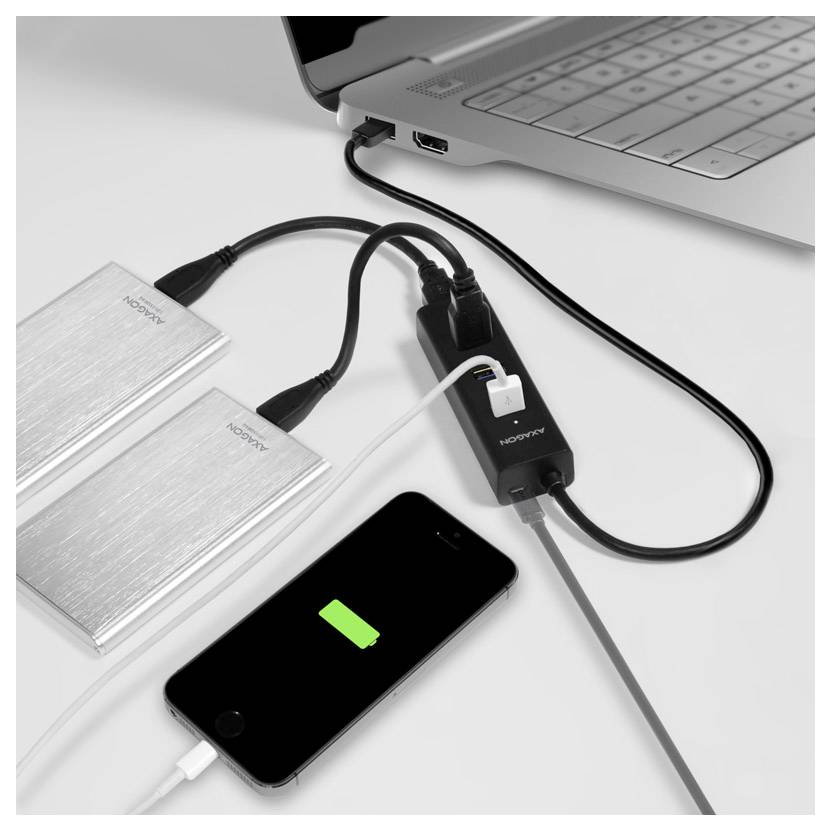 Prijenosno računalo spojeno na dva vanjska pogona i pametni telefon koji se puni preko USB huba na bijelom stolu.