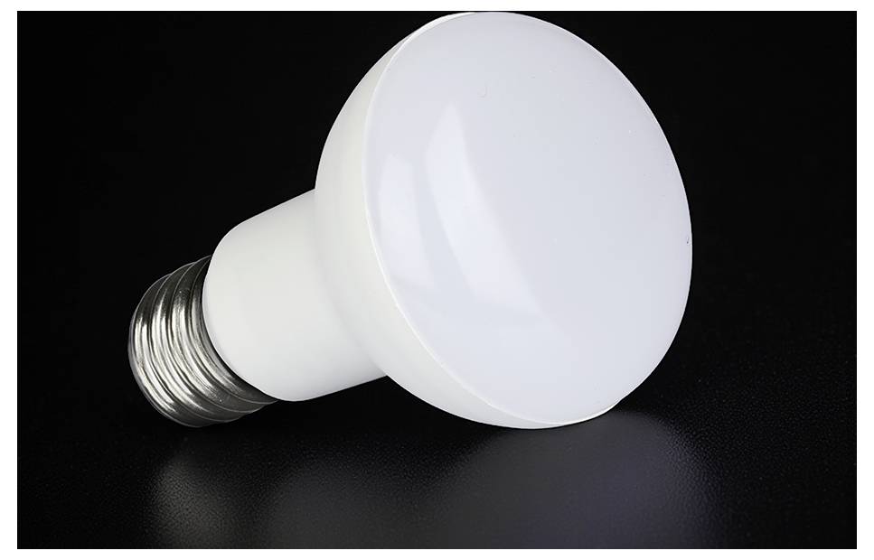 Bijela LED žarulja koja leži na tamnoj površini ispred crne pozadine.