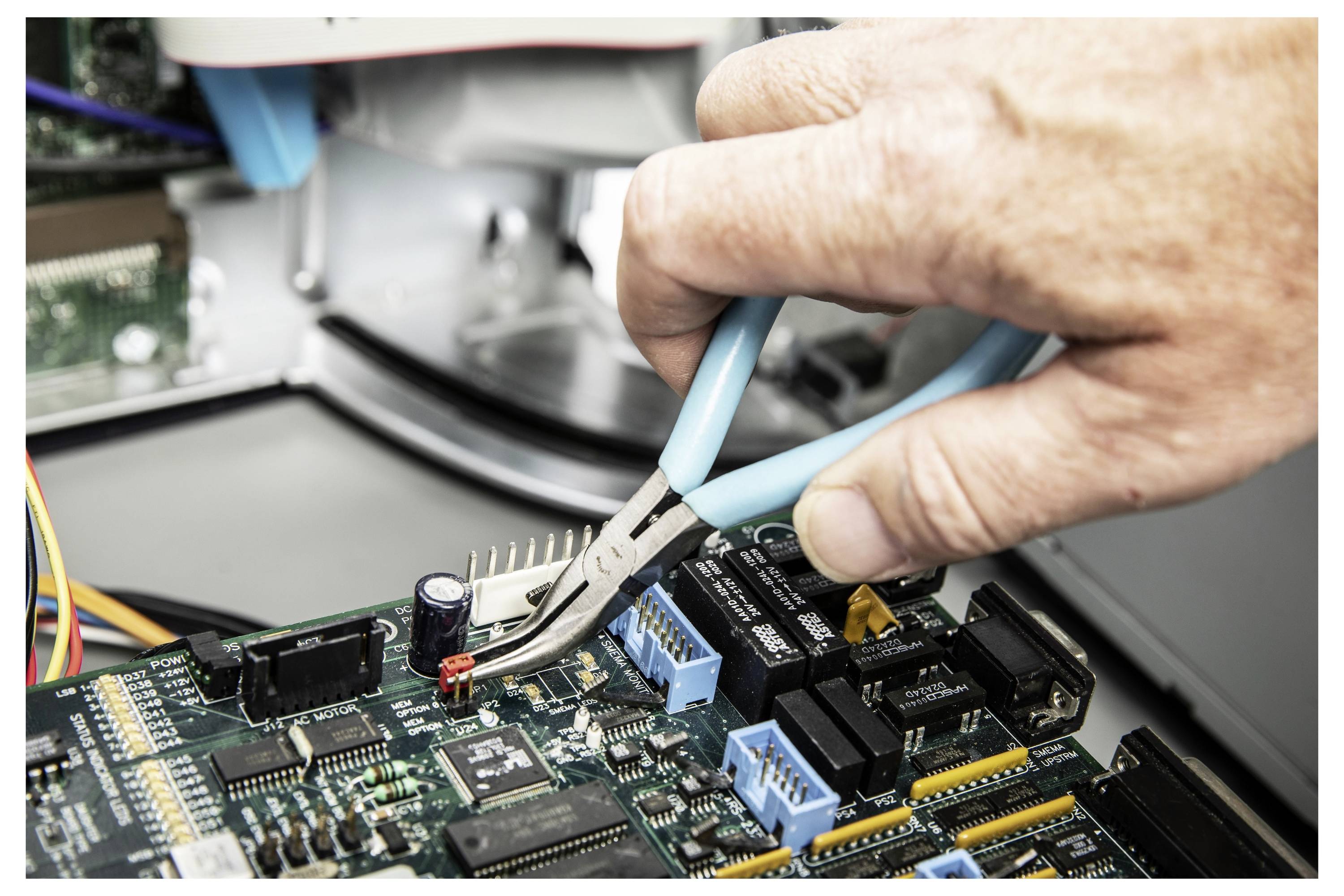 Ruka koristi kleštice za podešavanje malog elektroničkog komponente na matičnoj ploči tijekom popravke računalnog hardvera.