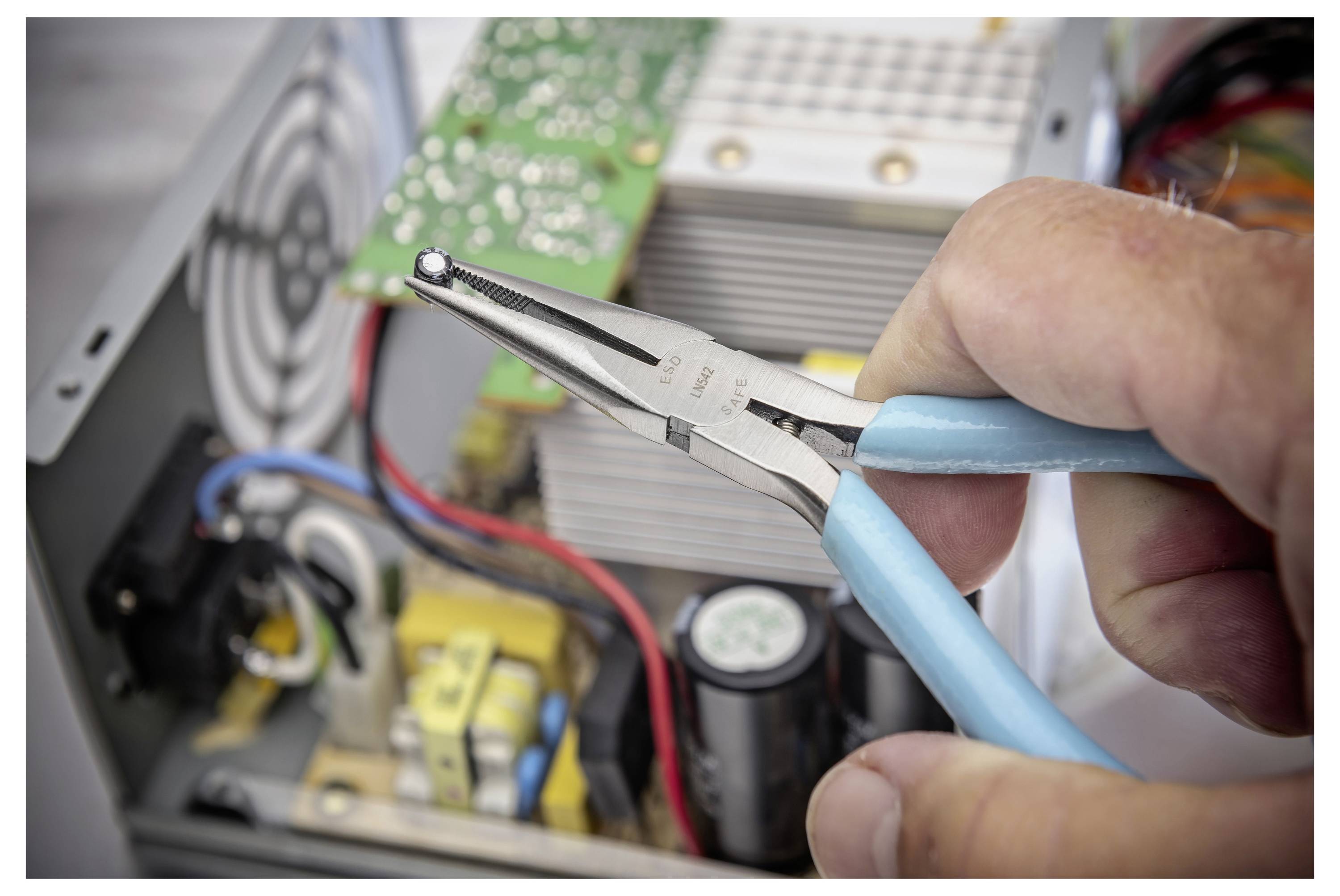 Ruka koja drži turpiju sa tankim vrhovima unutar otvorenog elektroničkog uređaja, radeći blizu ploča s integriranim sklopovima, žica i ventila za hlađenje.