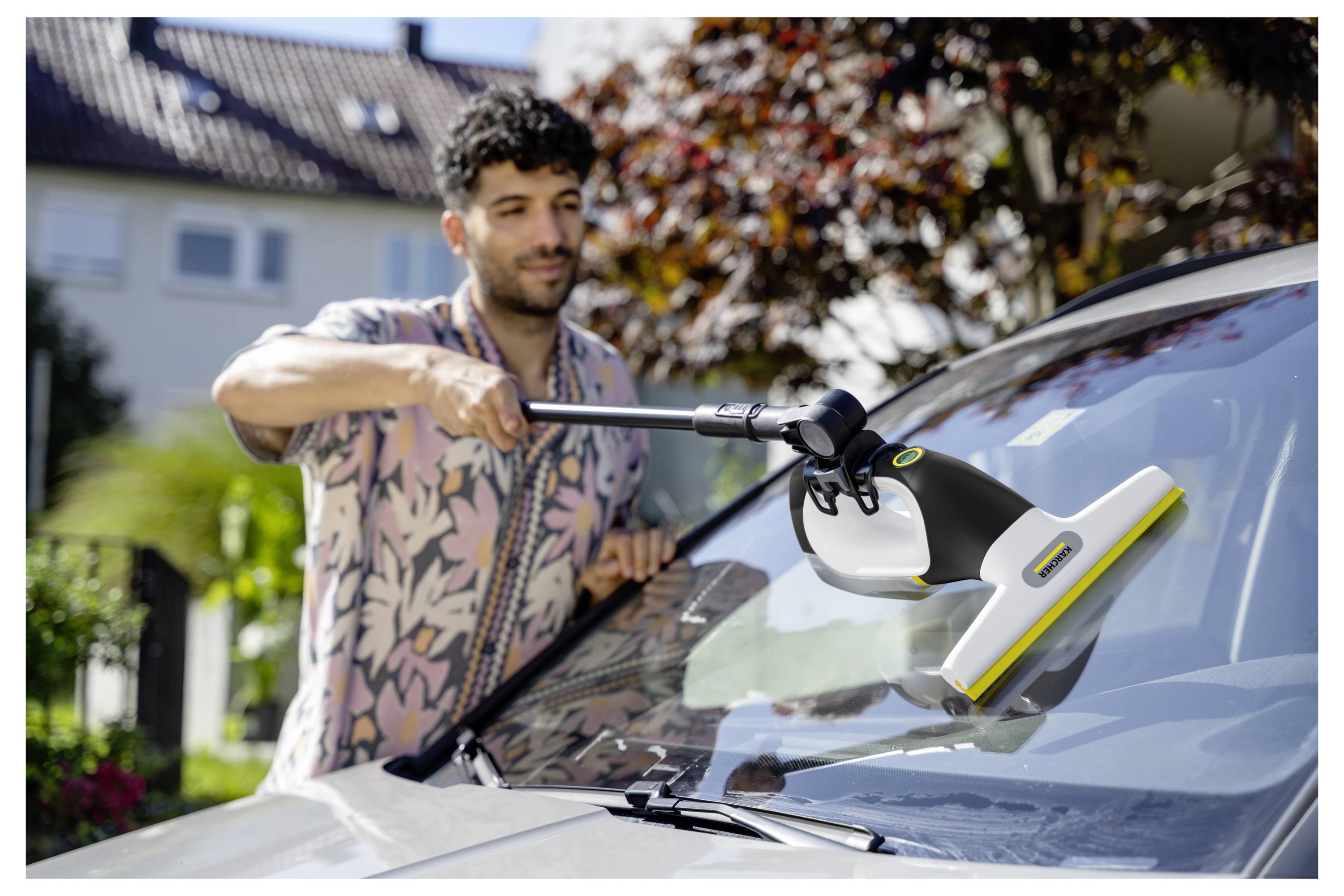Čovjek koristi alat za čišćenje vjetrobrana na prednjoj vjetrobranskoj ploči automobila u prizemljenju predgrađa.