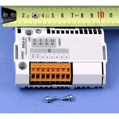 Bijeli elektronički modul na plavoj površini s mjernom trakom iznad njega i dva mala vijka ispod, prikazujući njegovu veličinu.