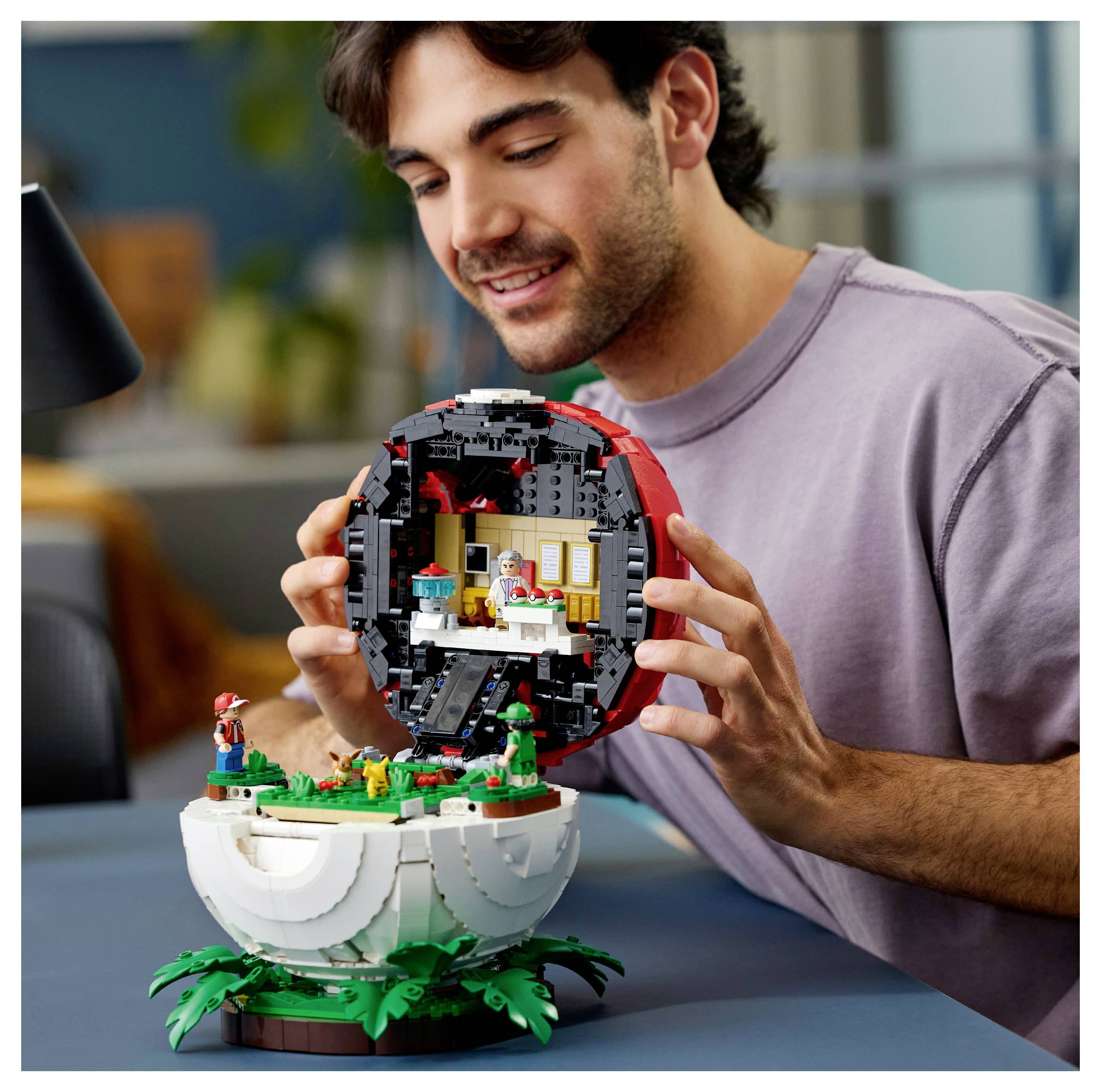 Muškarac se smješti dok drži otvoren model školjke u LEGO stilu na stolu, otkrivajući malu interijurnu scenu u njezinu unutrašnjosti.