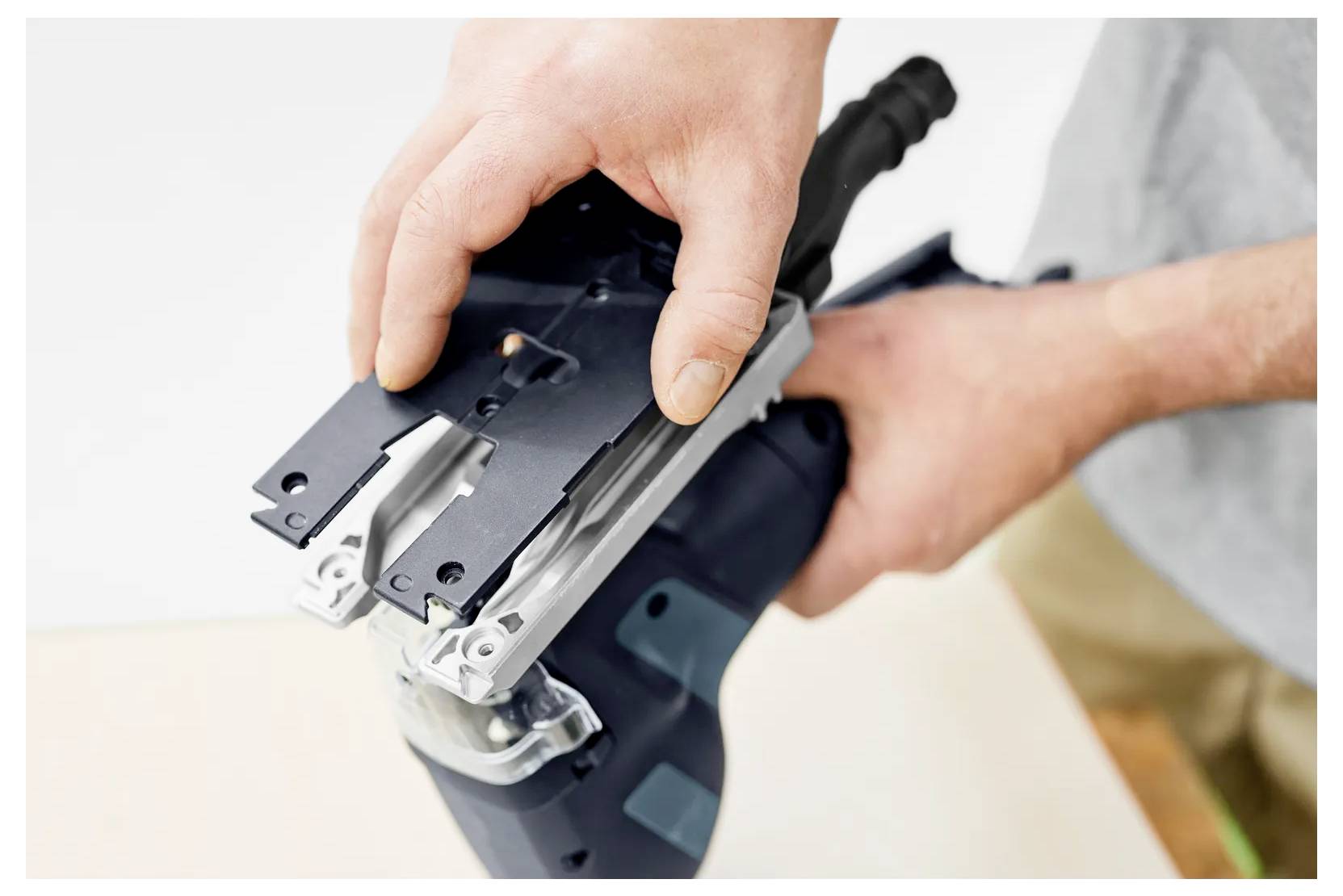 Ruke koje postavljaju električni alat, vjerojatno ubodnu pilu, dok montiraju ili mijenjaju njen nastavak za oštricu.